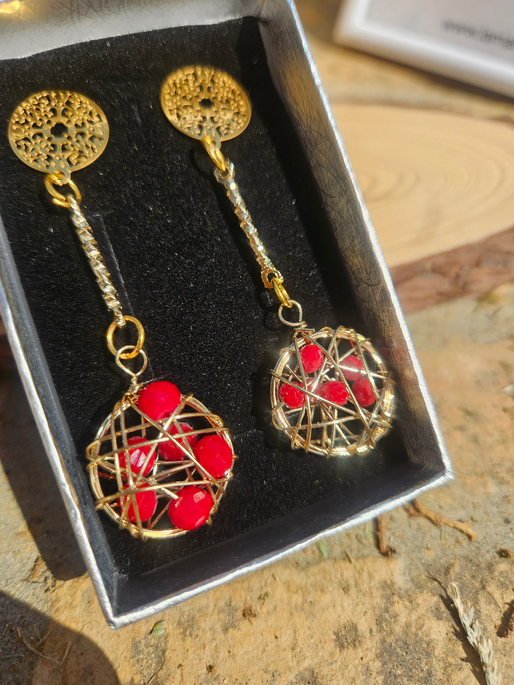 Pendientes colgantes con base dorada y esfera roja de hilo metálico.