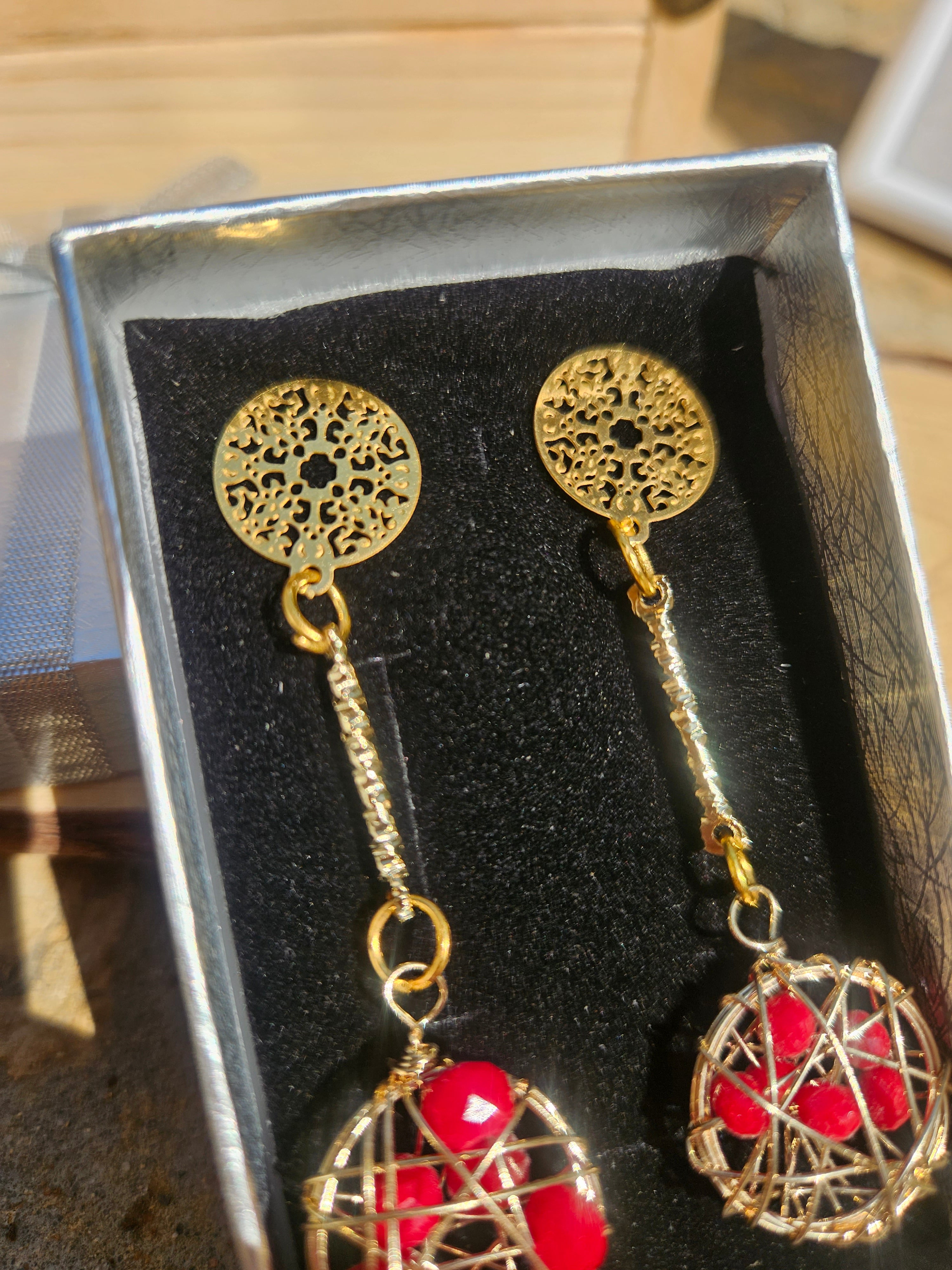Pendientes dorados con discos calados y esfera roja tipo globo colgante.