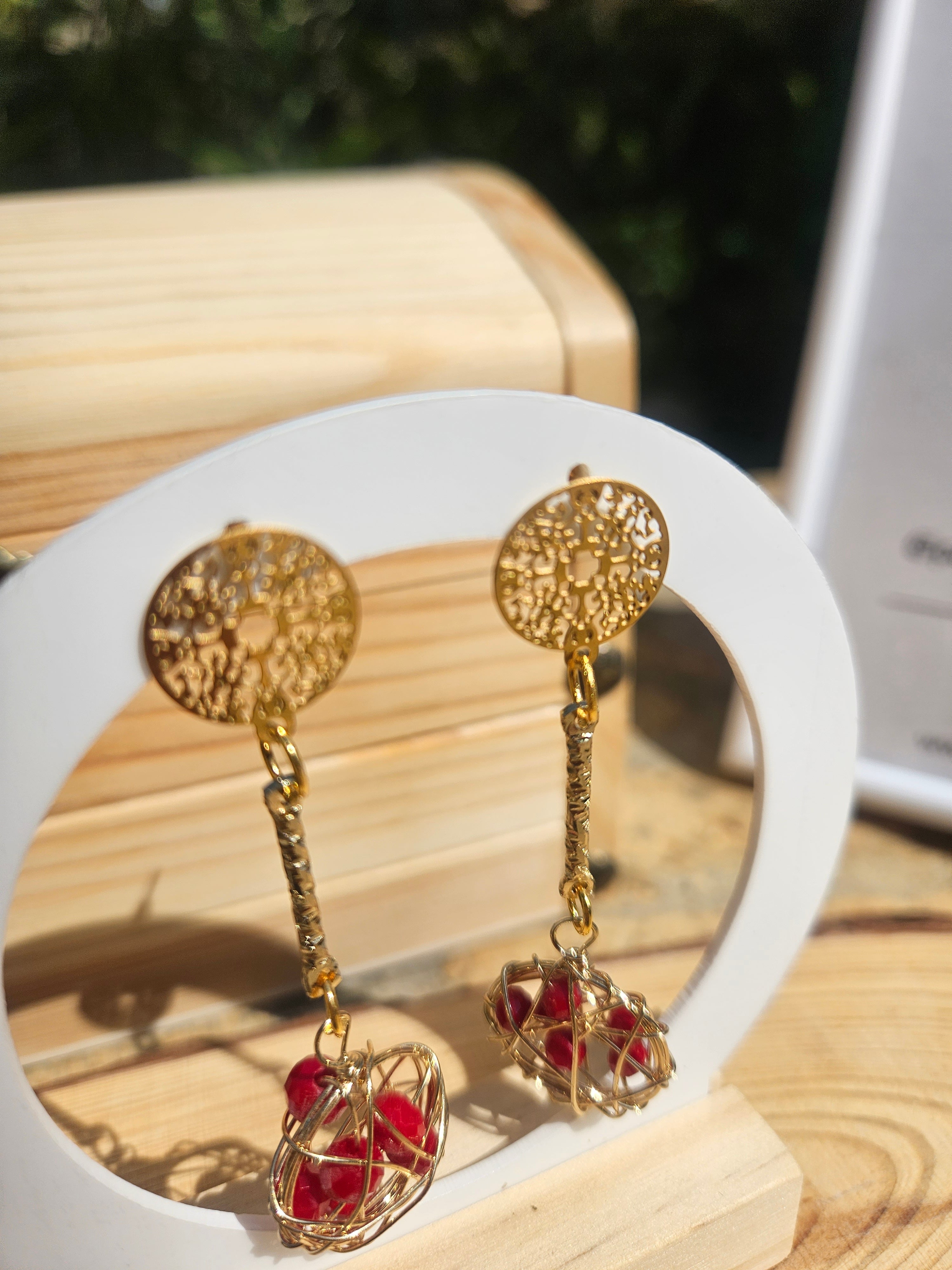 Pendientes dorados con discos calados y esferas rojas de alambre.