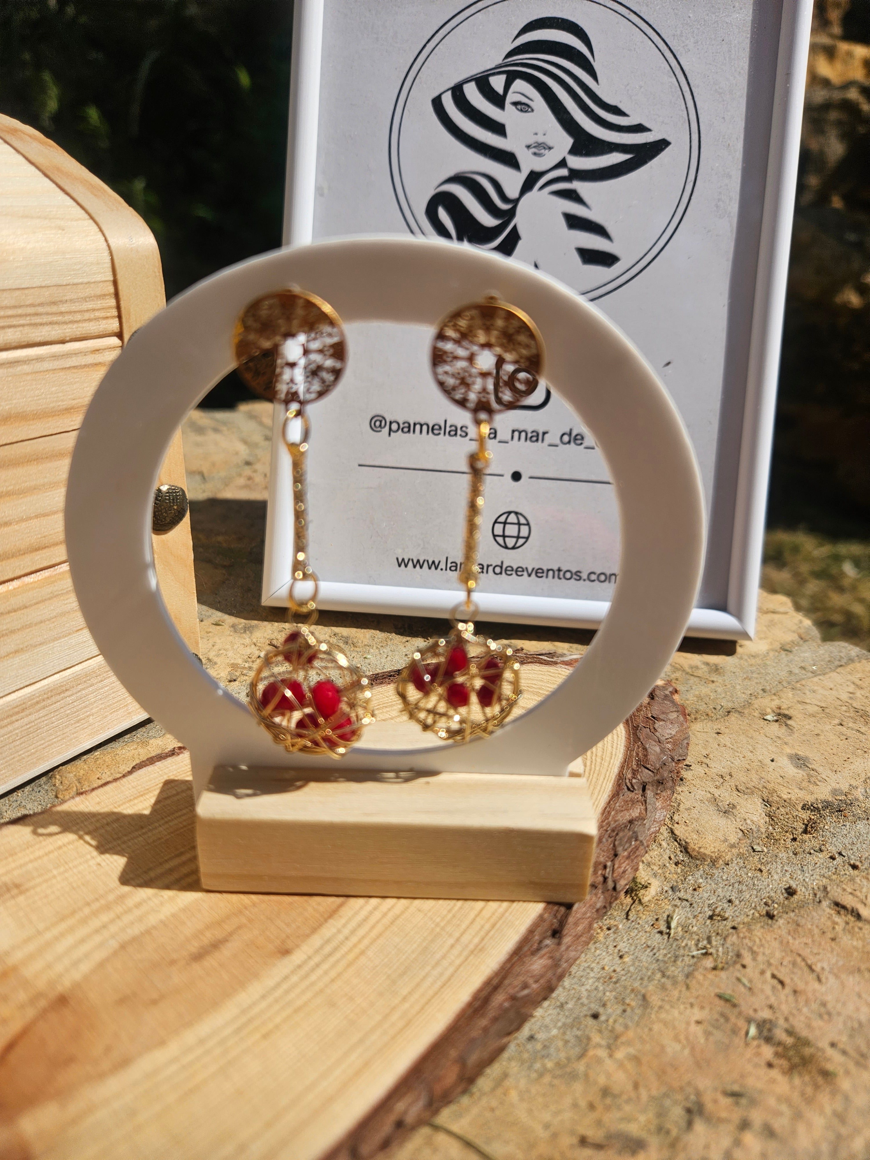 Pendientes dorados con esfera roja tipo globo y cuentas rojas colgantes.