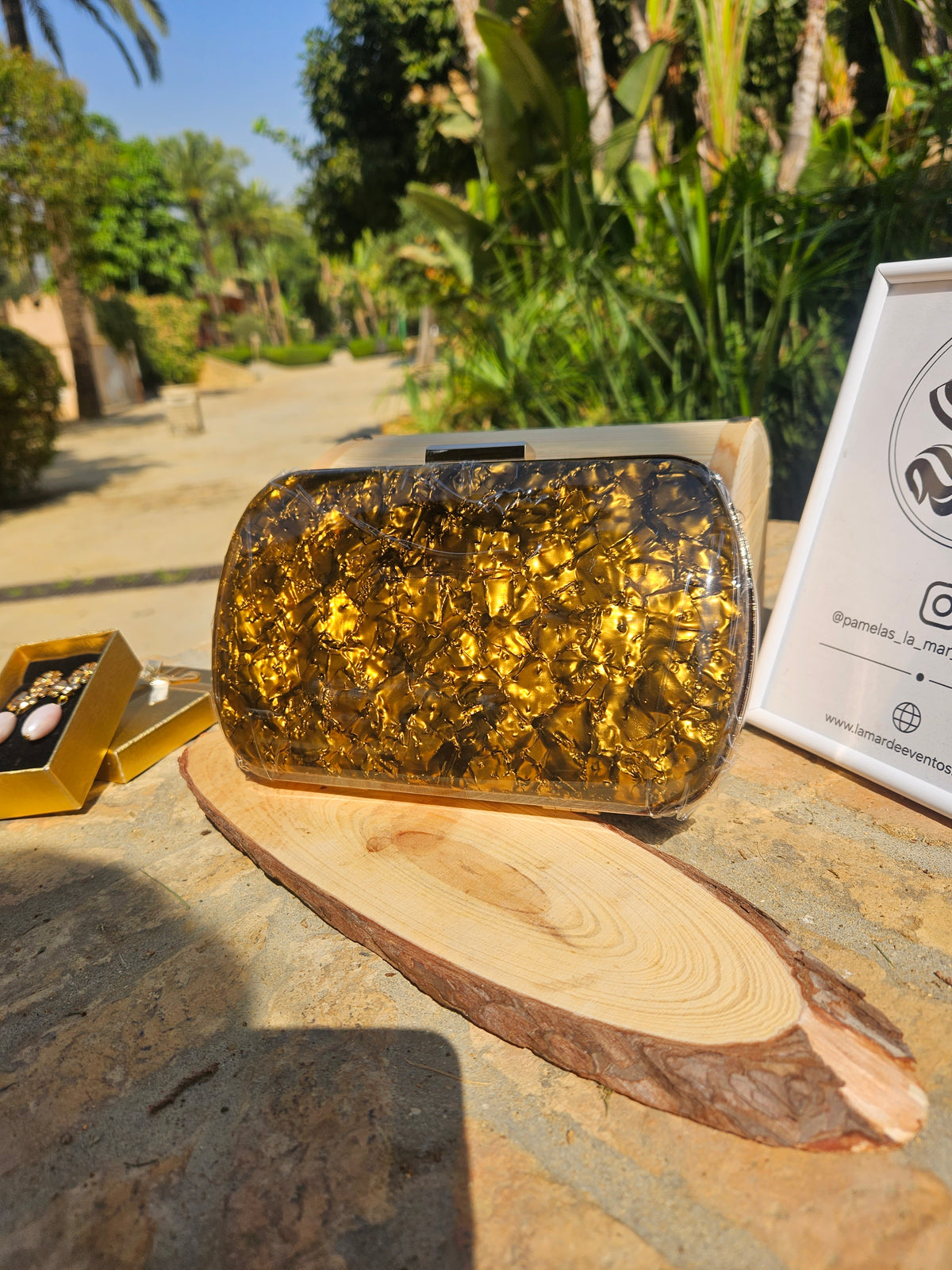 Bolso de mano dorado brillante con asa superior y cierre metálico sobre base plana