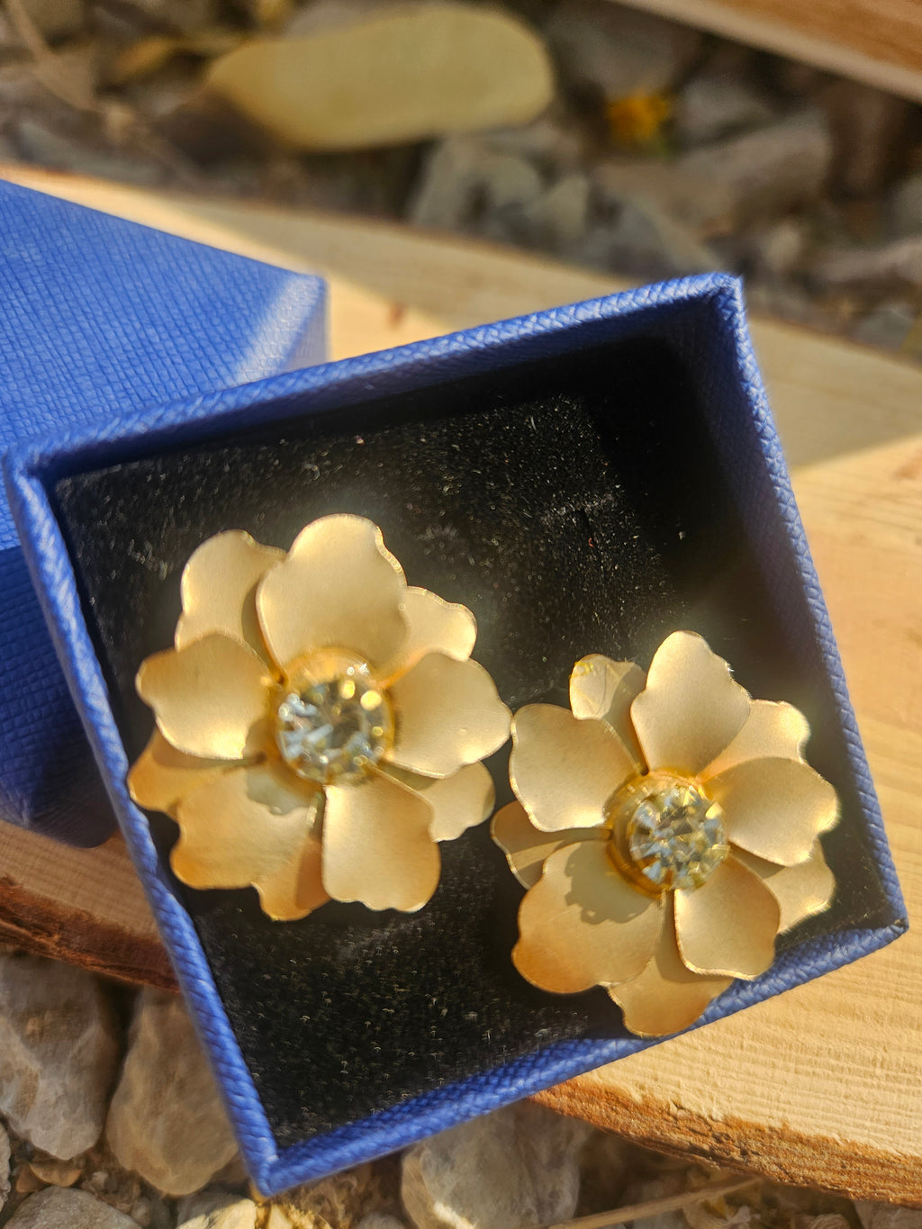 Pendientes con flores doradas y pedrería circular, vista de cerca en caja negra