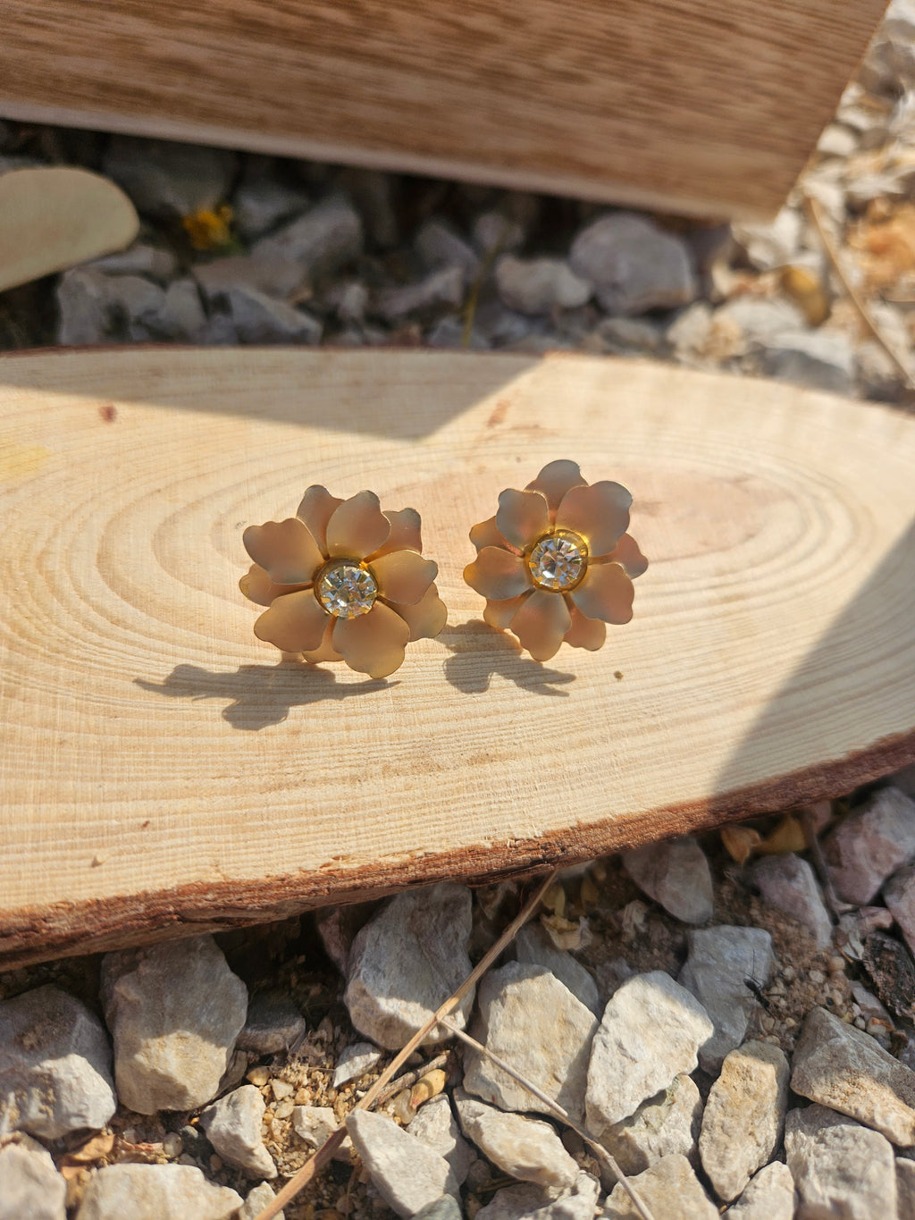 Pendientes con flores doradas y pedrería central, colocados sobre tablón de madera
