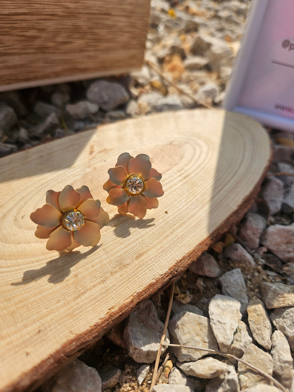 Pendientes con flores doradas y pedrería central, vistos sobre trozo de madera