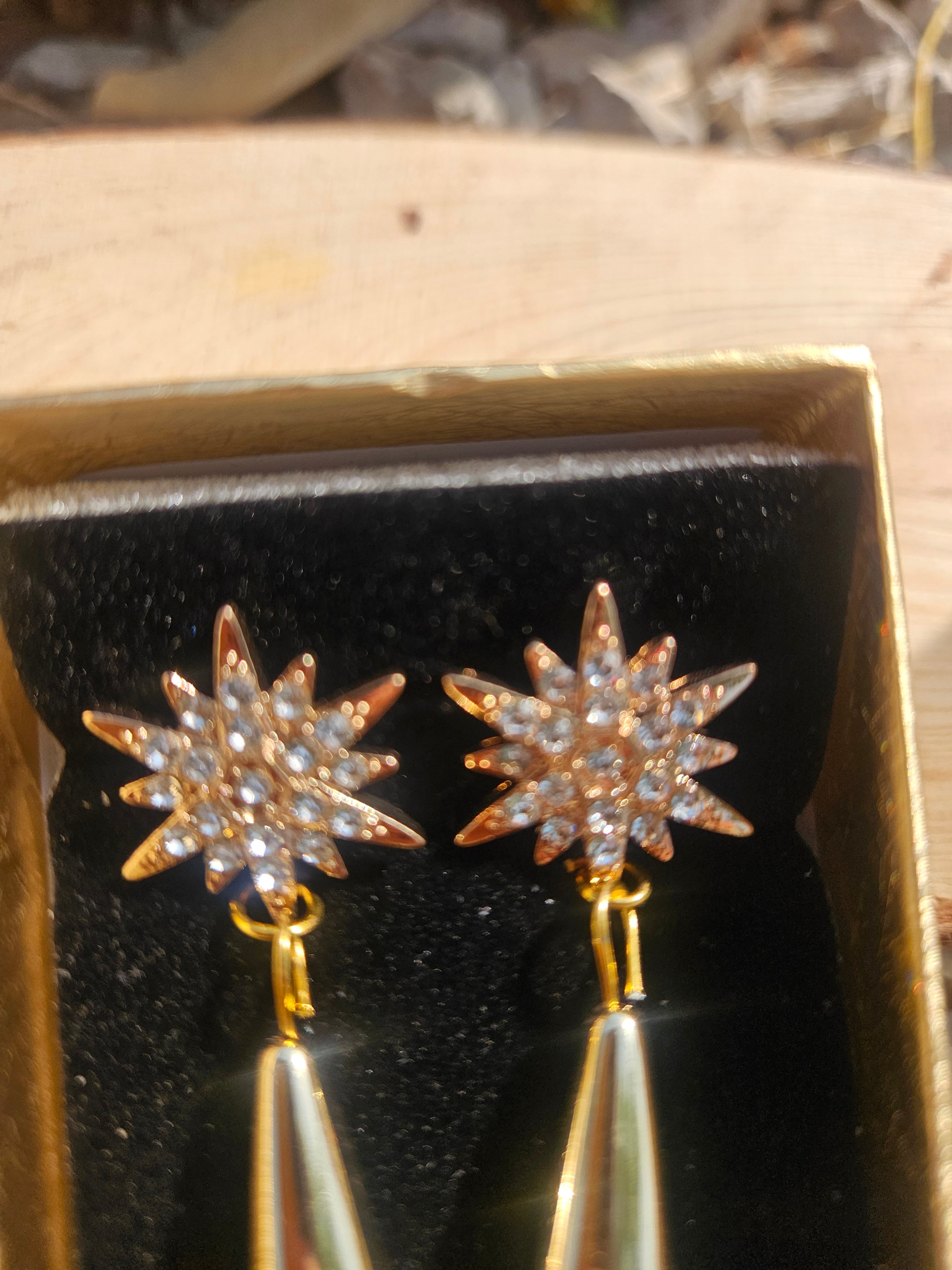 Pendientes dorados con flores tipo estrella y colgantes lágrima, en caja negra.