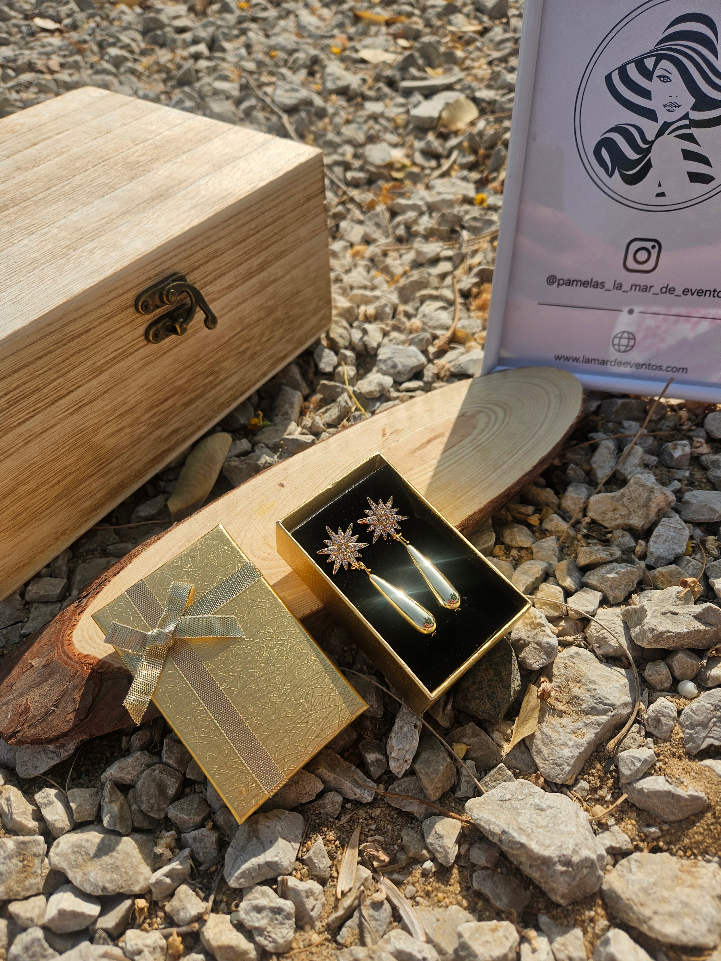 Pendientes dorados con estrellas engastadas y colgantes lágrima, junto a caja y lazo.