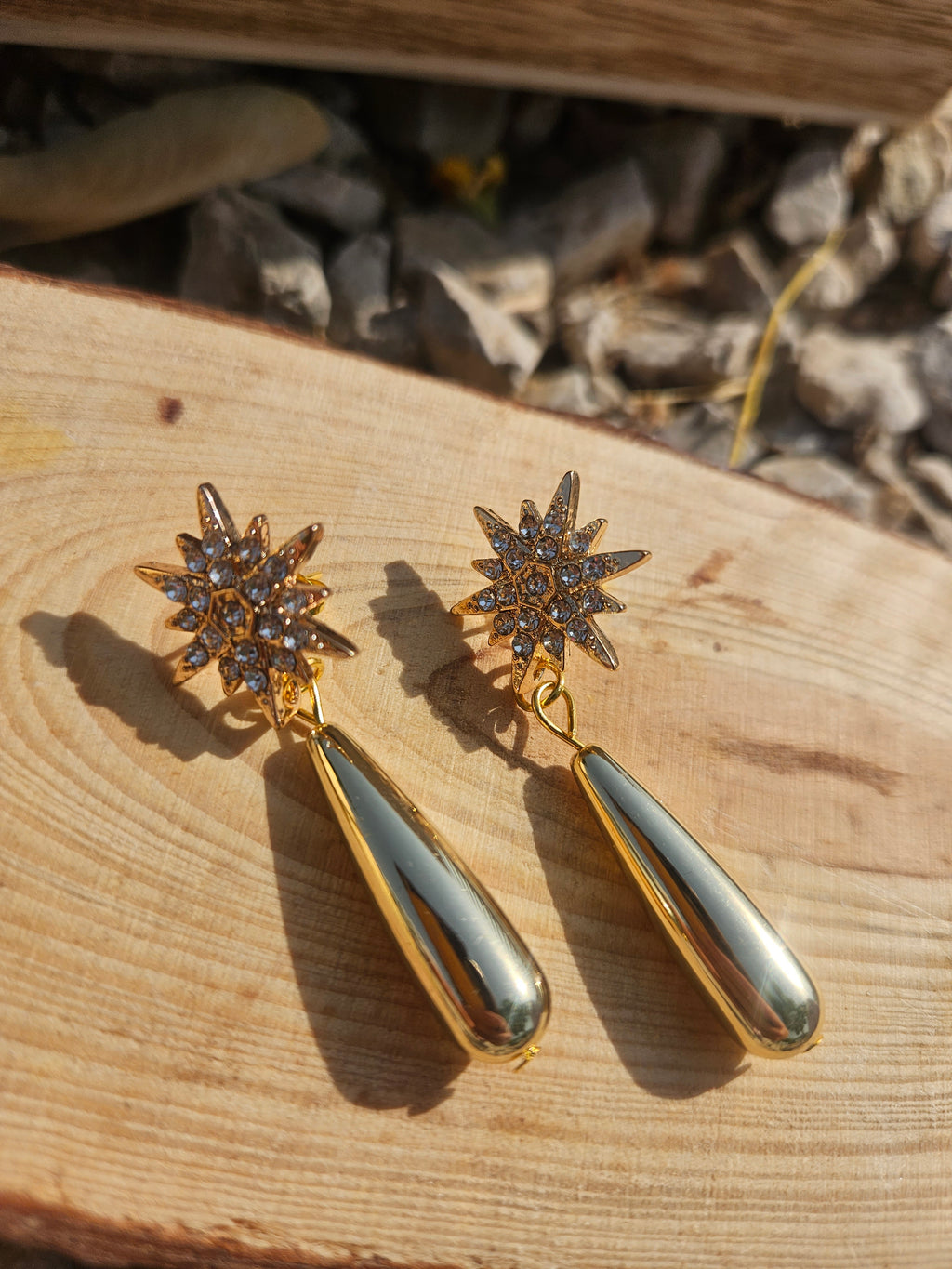 Pendientes colgantes dorados con estrellas engastadas y colgante lágrima ovalada brillante.