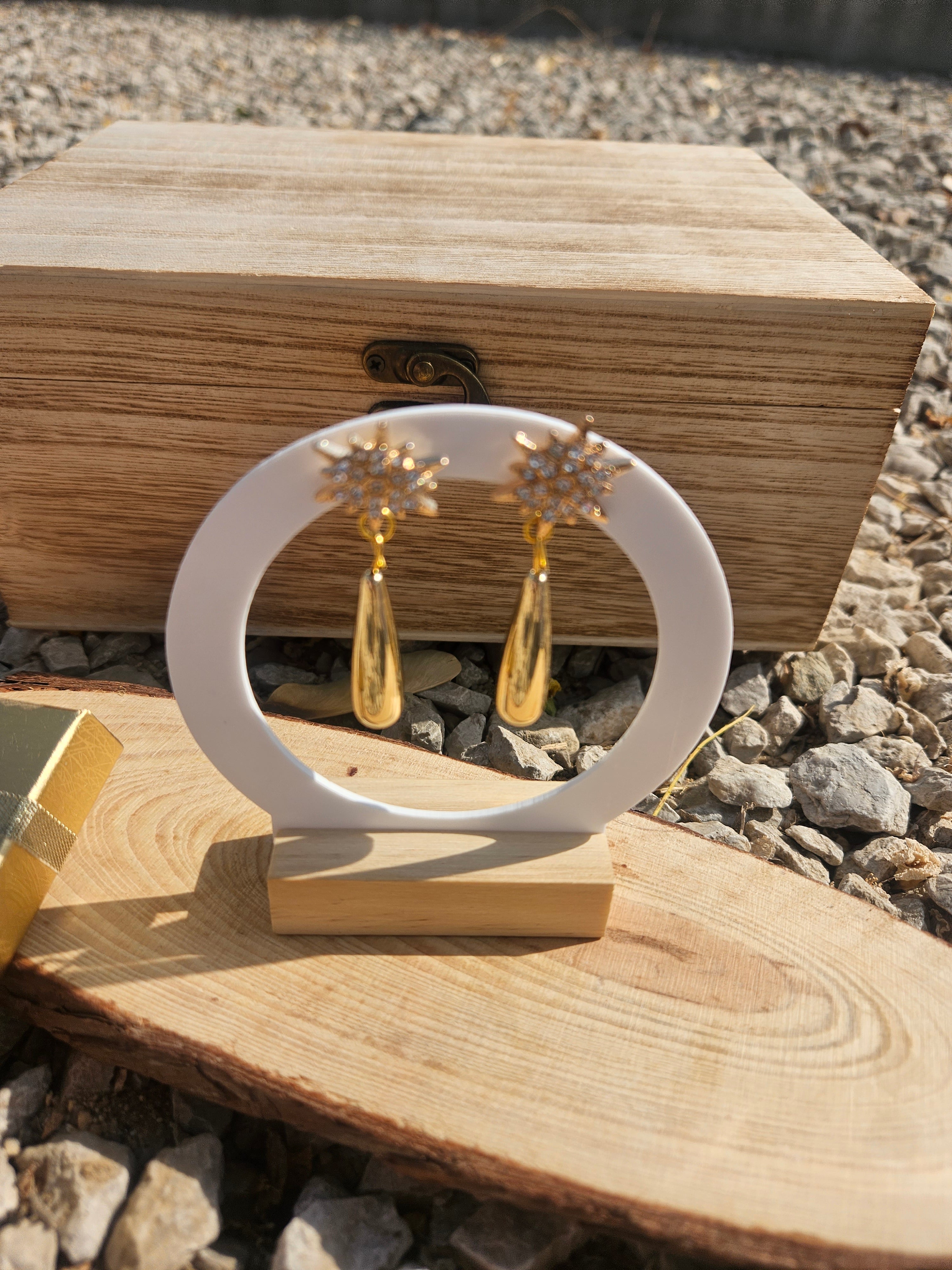 Pendientes dorados con estrellas y colgantes lágrima, en soporte blanco sobre madera.