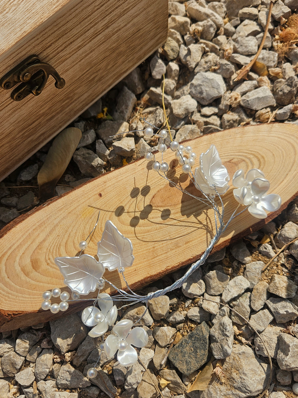 Tiara de novia plateada con flores blancas, perlas y ramita curva sobre fondo de madera