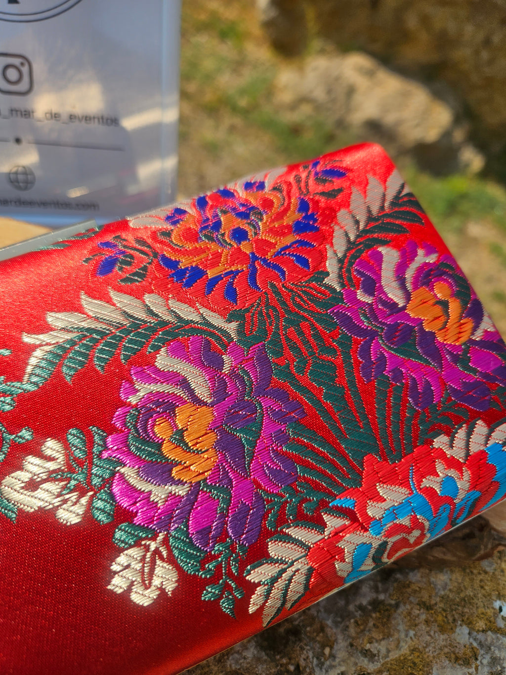 Bolso rojo con bordado floral multicolor sobre tela brillante.