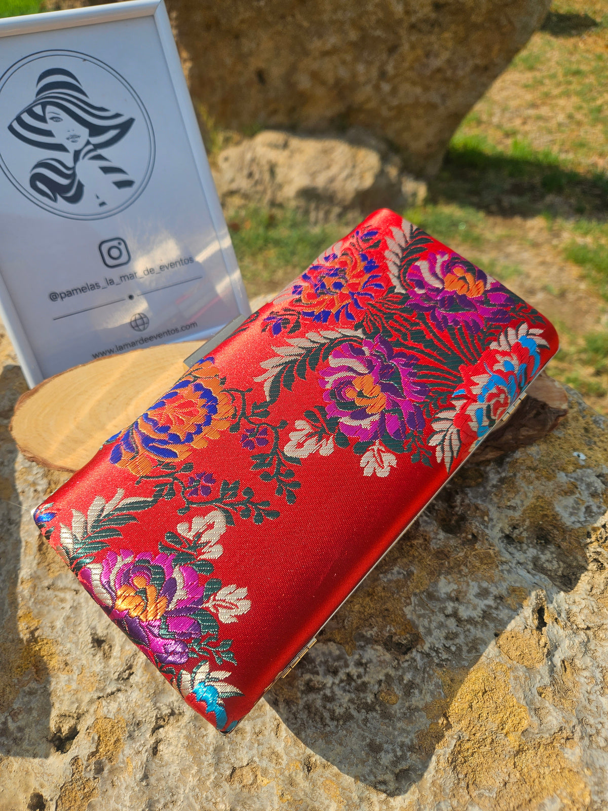 Bolso tipo clutch rojo con bordado floral multicolor y marco metálico dorado.