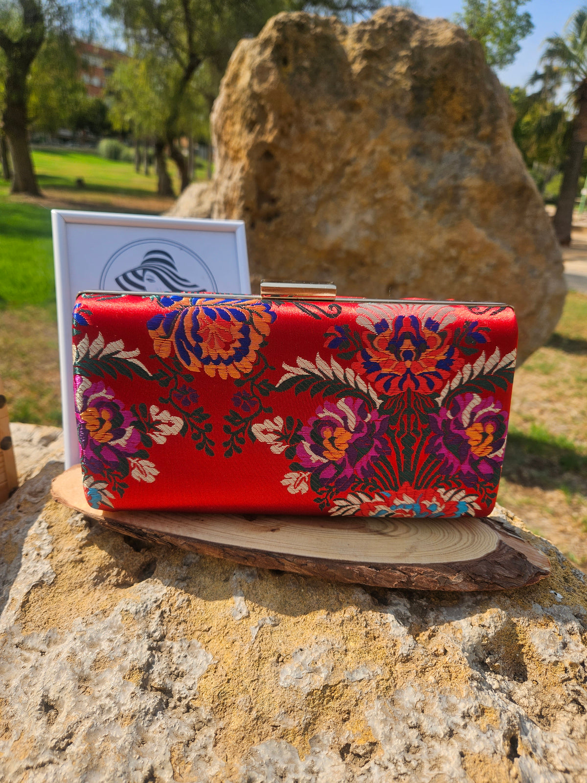 Bolso tipo clutch rojo con bordado floral multicolor y marco rígido metálico dorado.