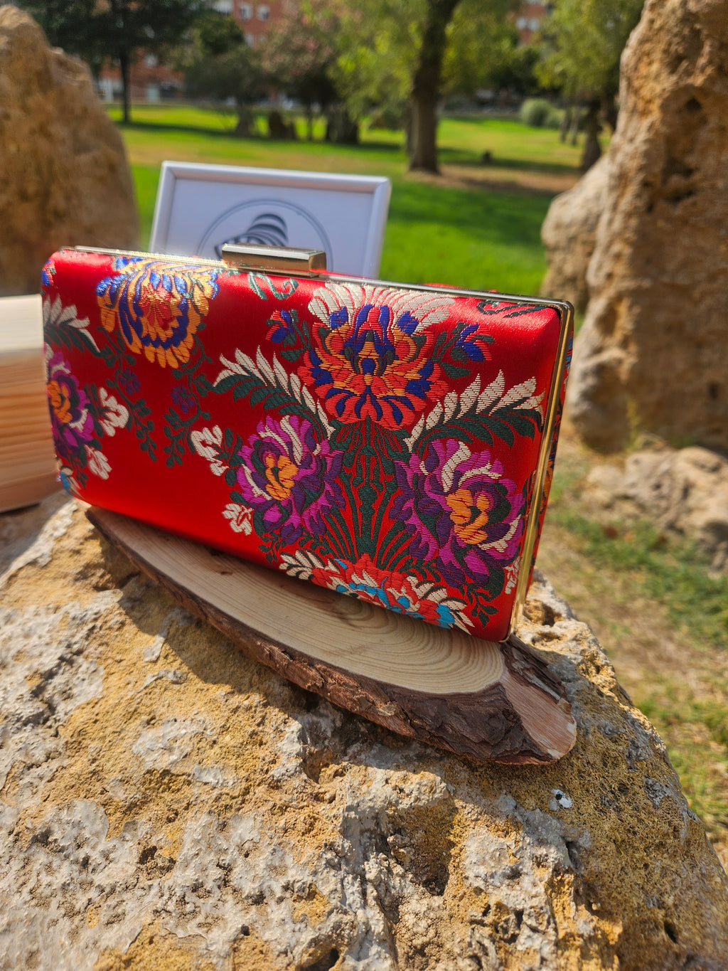 Bolso clutch rojo con bordado floral multicolor y cierre metálico en la parte superior.