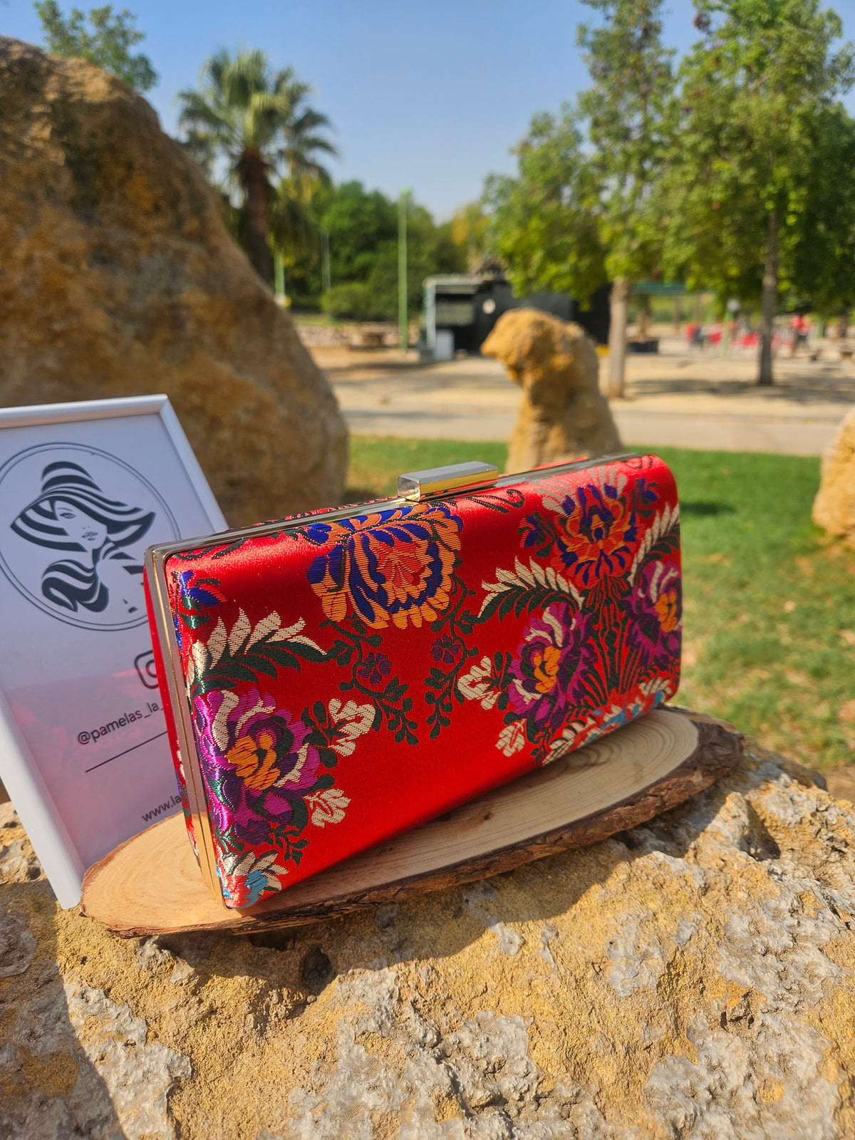Bolso rojo con bordado floral multicolor y marco rígido metálico dorado.