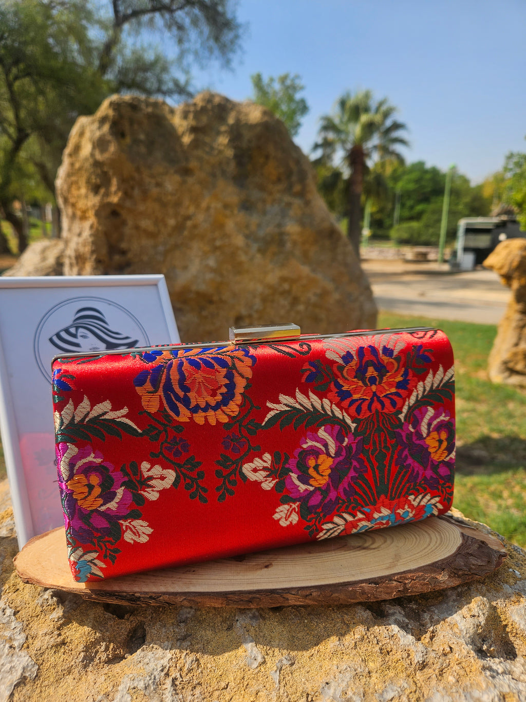 Bolso tipo clutch rojo con bordado floral multicolor y herraje metálico brillante.