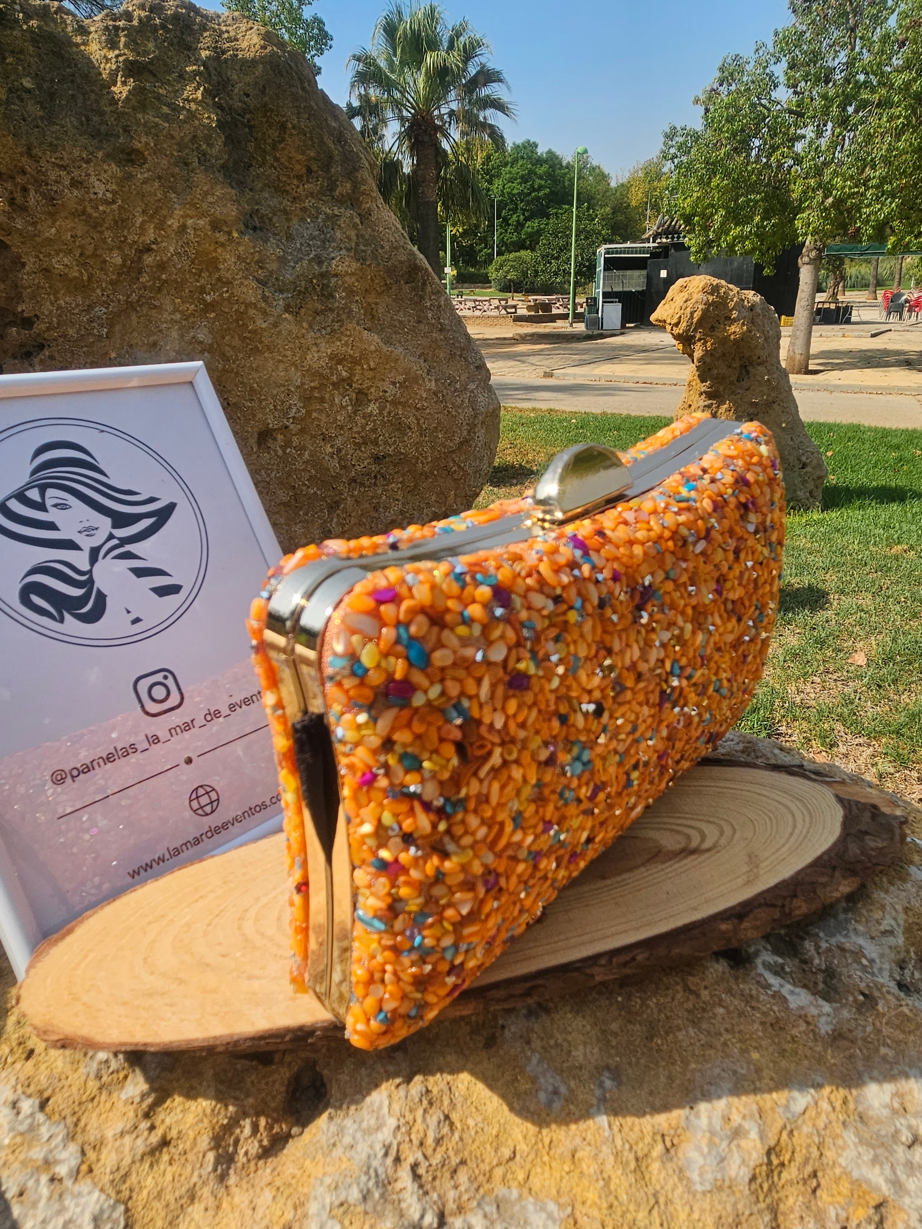 Bolso de cuentas naranja multicolor con asa superior y cierre metálico, vista lateral.