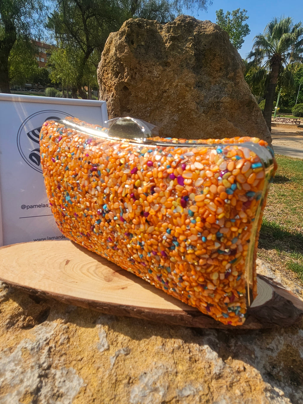 Bolso de cuentas naranjas y azules con asa redonda metálica, vista trasera.