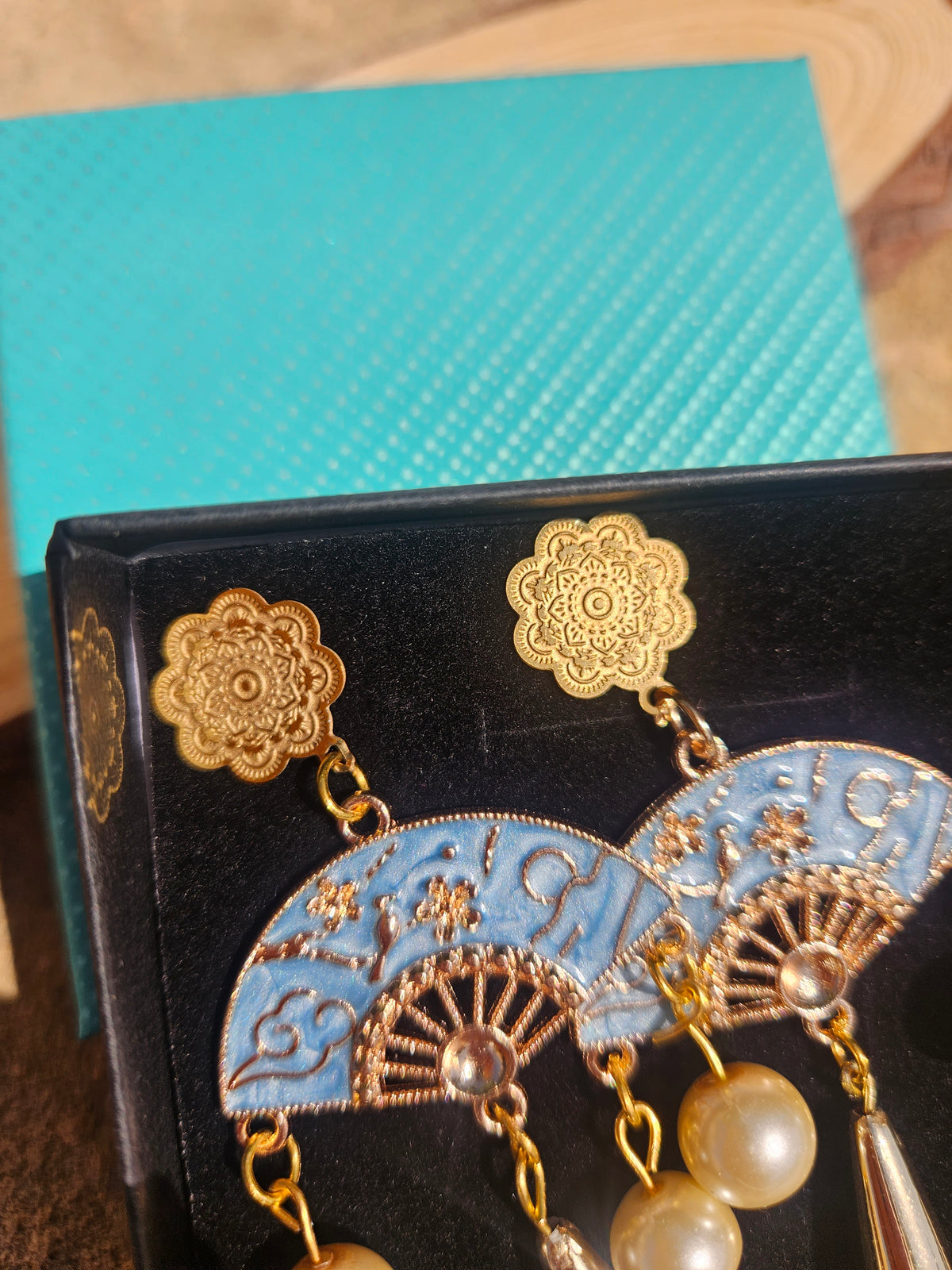 Pendientes en caja negra: flores doradas, medallones azules y perlas con gota metálica