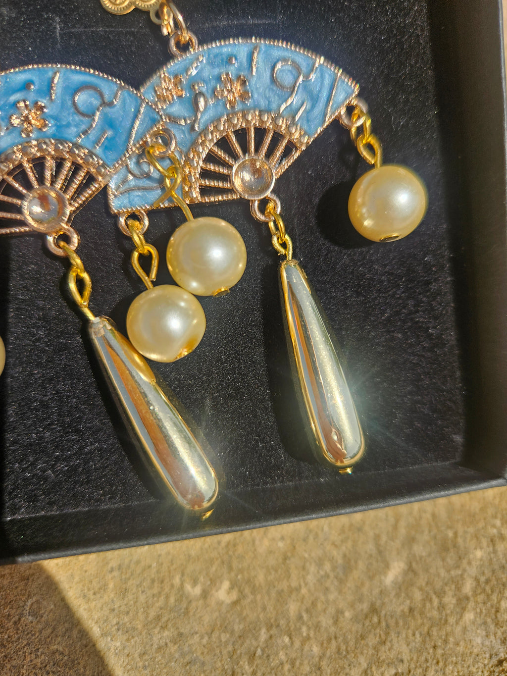 Detalle de pendientes: medallones azules, cadenas doradas, perlas y colgantes de gota