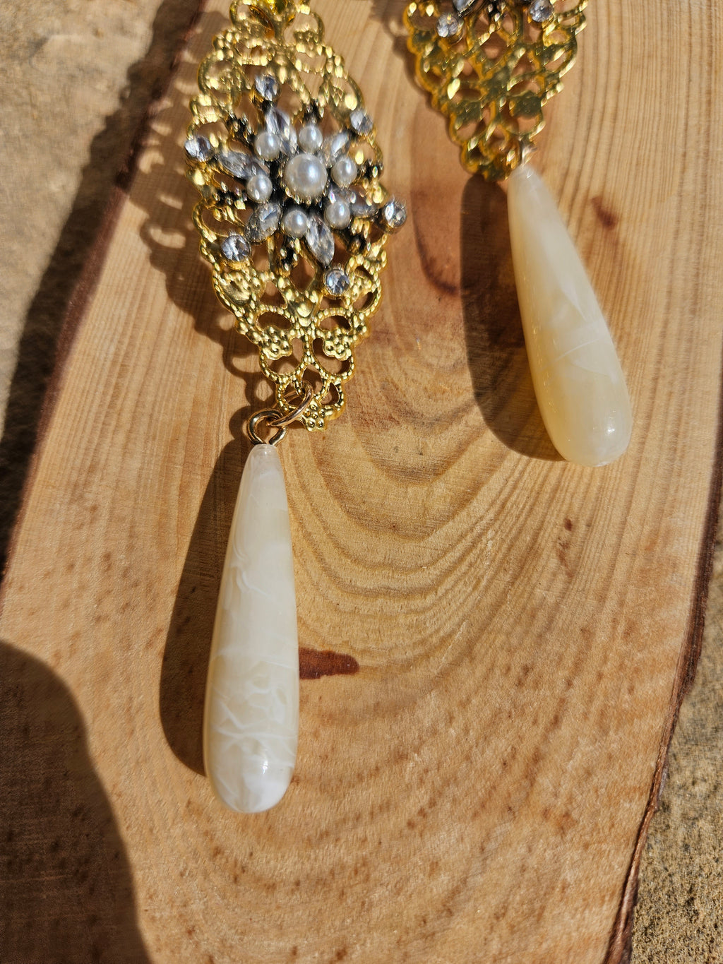 Detalle de pendientes dorados con pedrería y gota colgante marfil