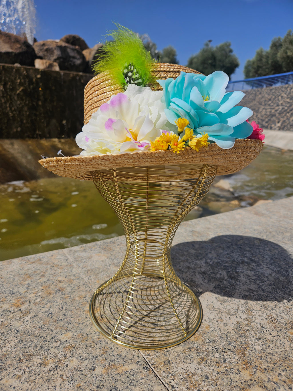 Sombrero de paja beige con flores blancas y azules, margaritas amarillas y pluma verde