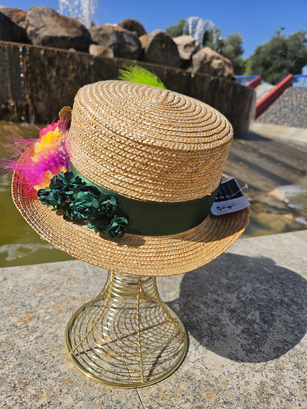 Sombrero de paja beige con banda verde y flores oscuras, con pluma verde