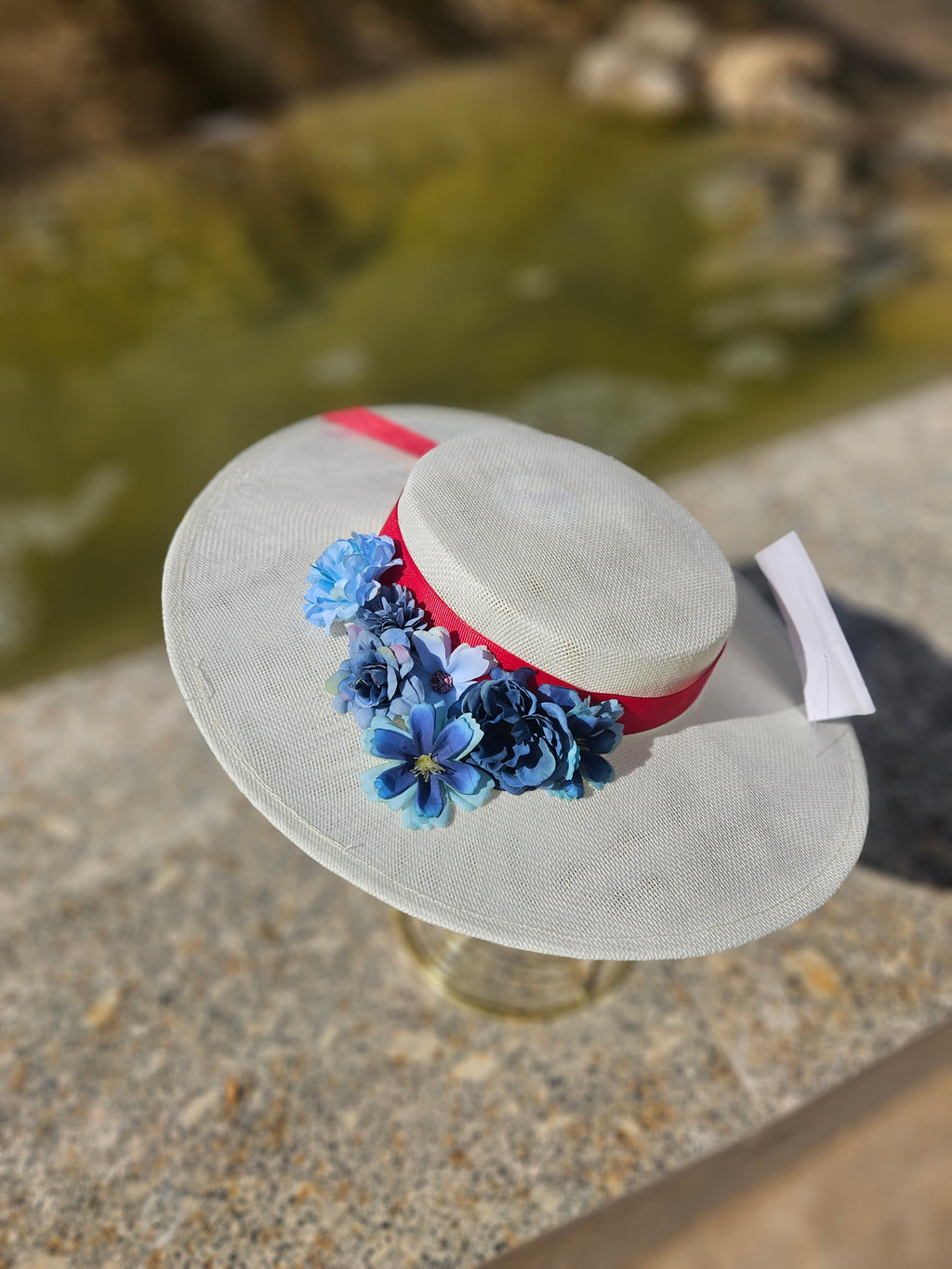 Pamela de ala ancha blanca con cinta roja y flores azules grandes, vista inclinada