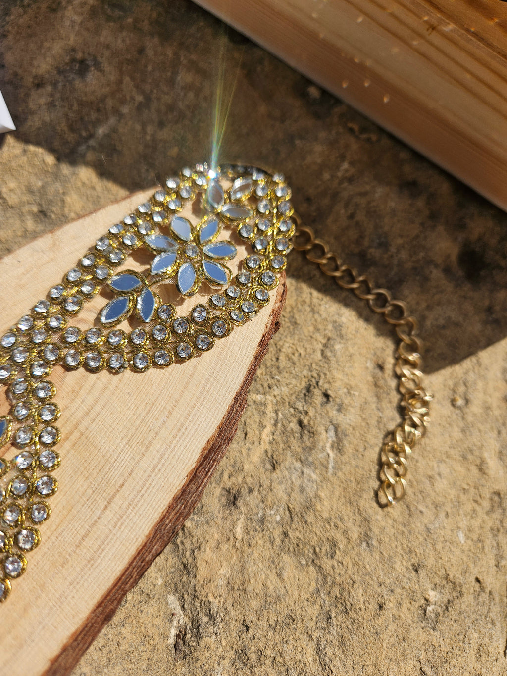Detalle de gargantilla dorada con piedras azules y patrón de hojas