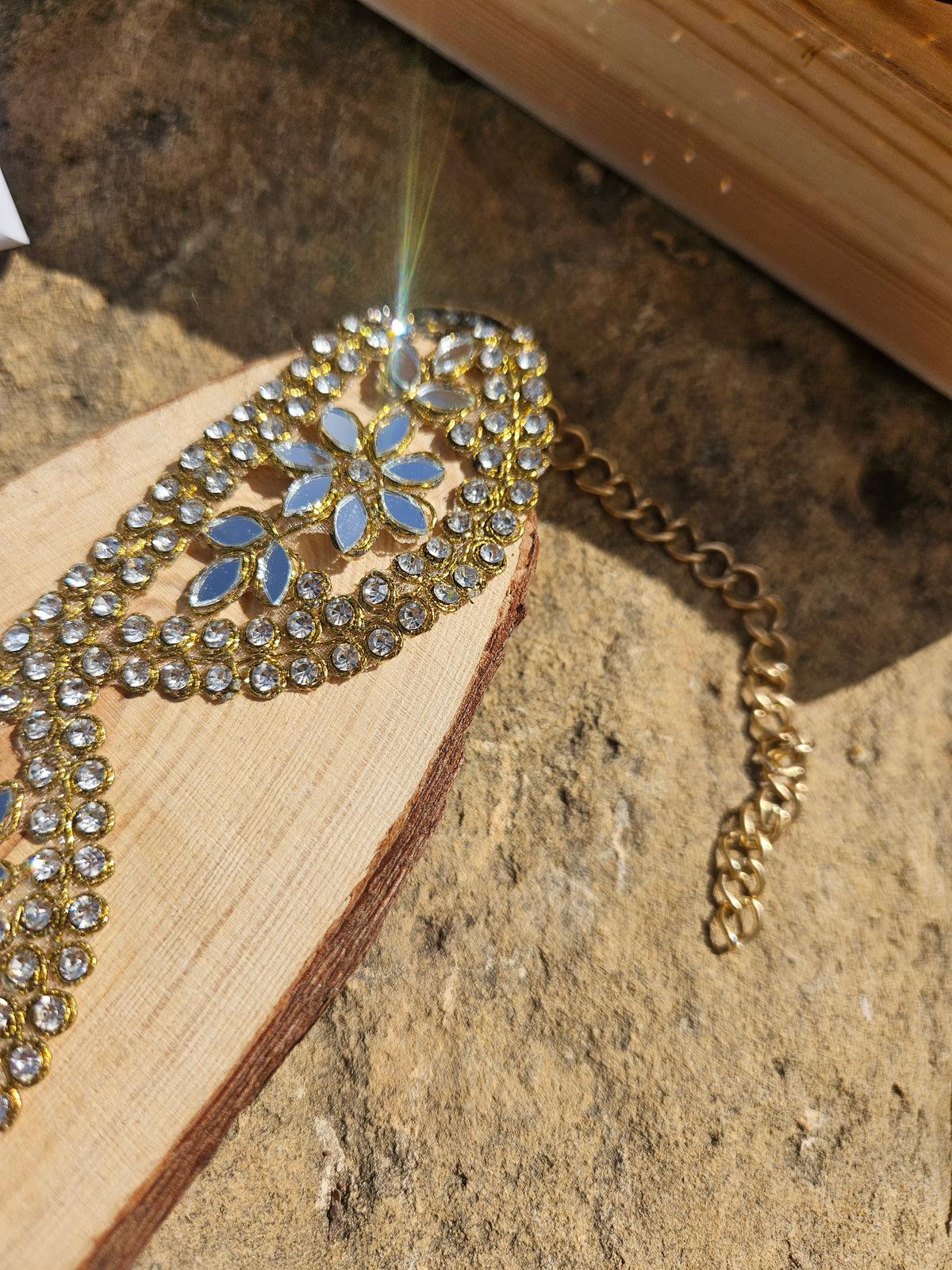 Detalle de gargantilla dorada con piedras azules y patrón de hojas
