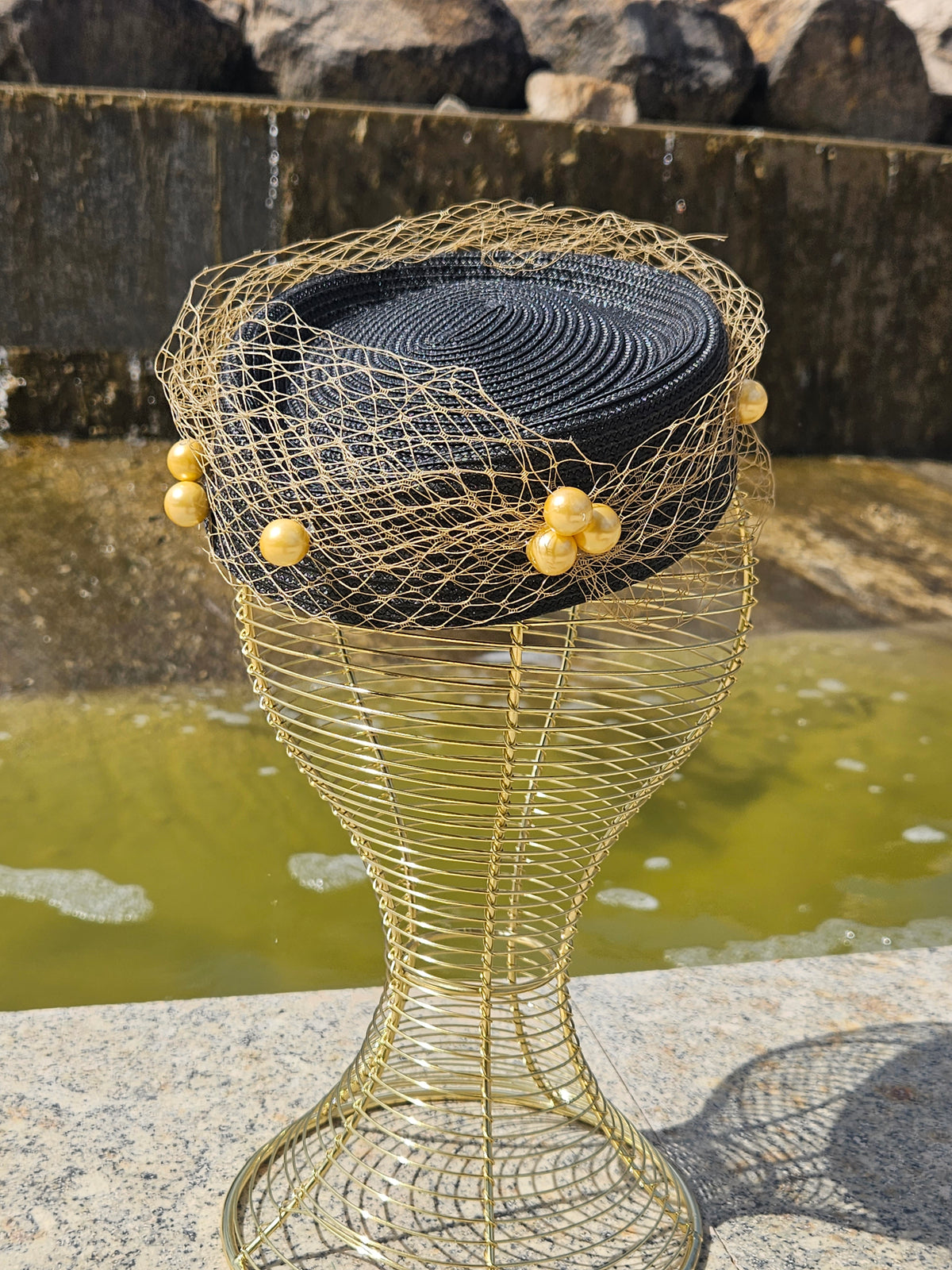 Sombrero fascinador de malla dorada con base negra y cuentas en el borde