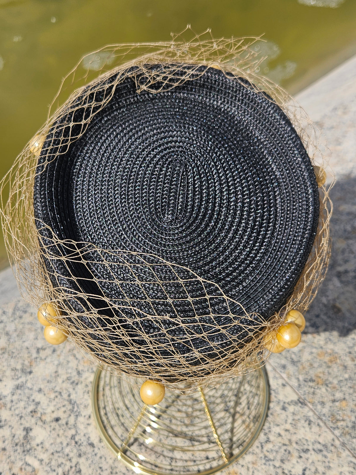 Detalle del sombrero: base negra circular con malla dorada y cuentas perladas