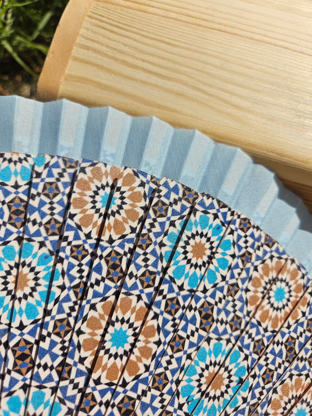 Abanico abierto con patrón geométrico azul y crema, detalles en naranja y forma semicircular.
