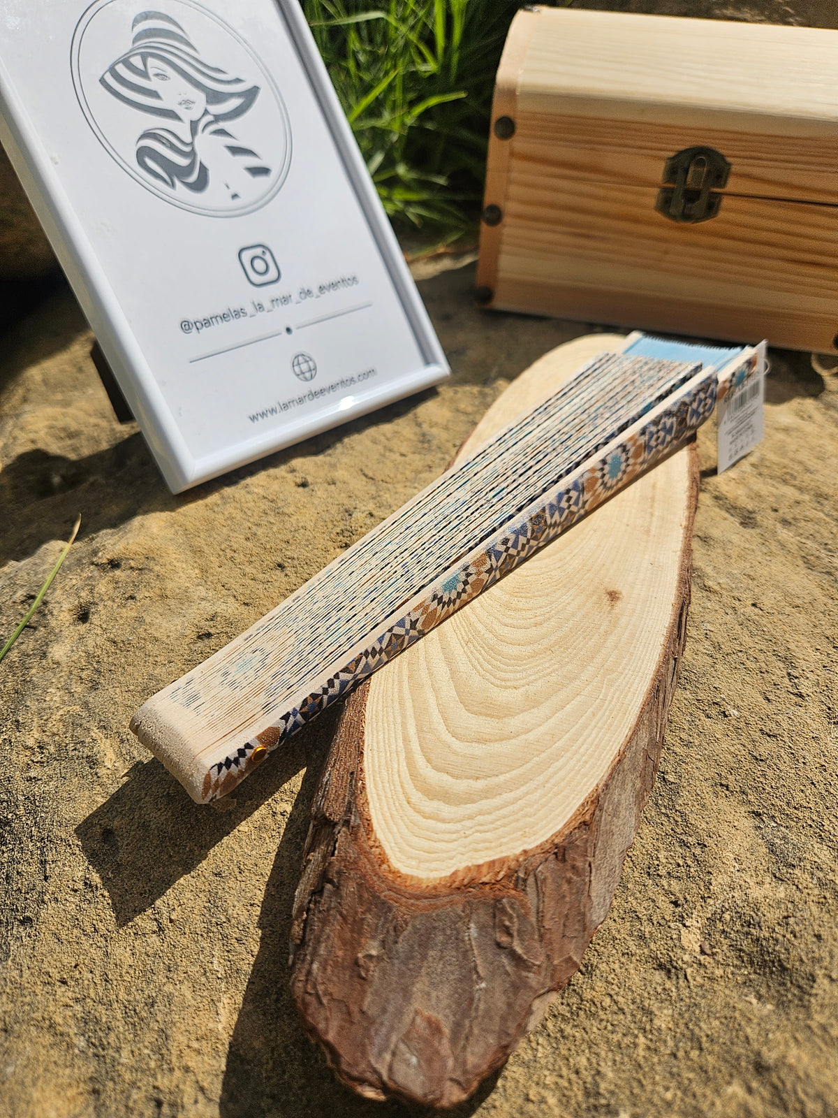 Abanico con banda geométrica azul y crema y estuche de madera, extendido parcialmente.