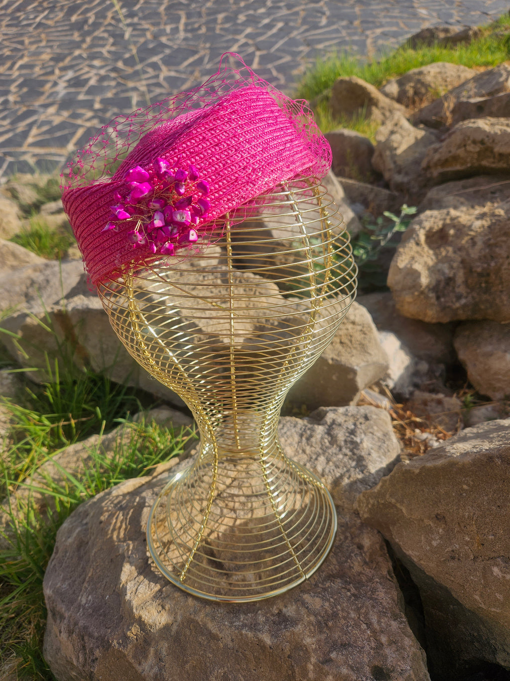 Sombrero fucsia tipo pillbox con velo de malla y adorno metálico sobre maniquí
