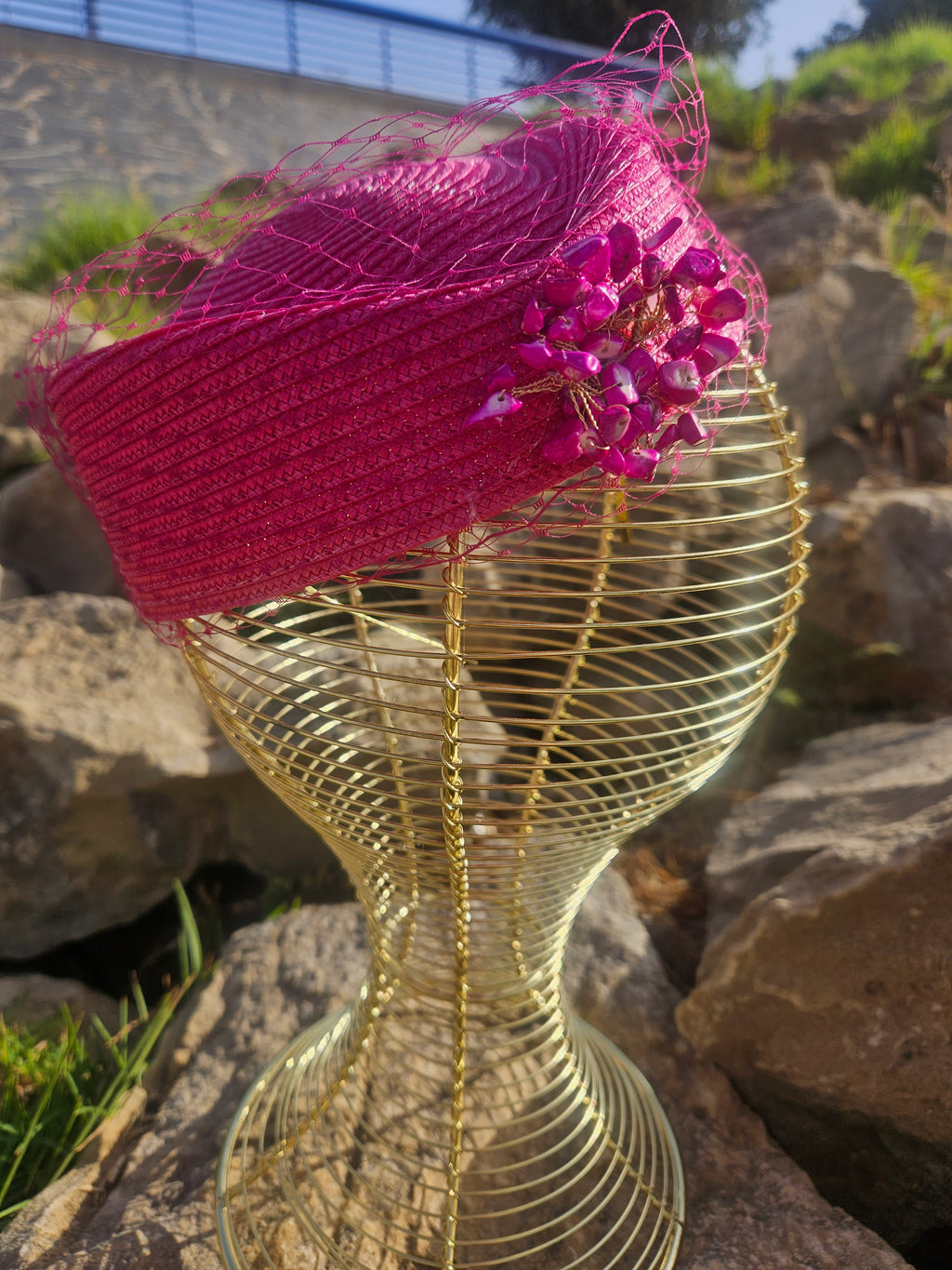 Sombrero fucsia inclinado con velo de malla y adorno floral brillante en el lateral
