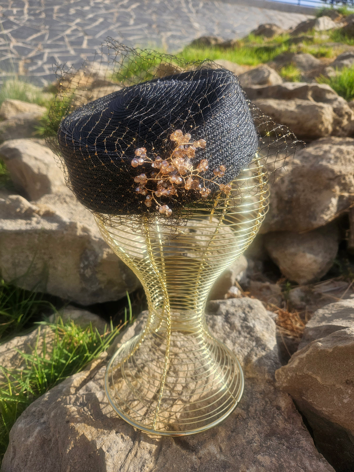 Sombrero de malla negro con pedrería y flor dorada sobre la copa