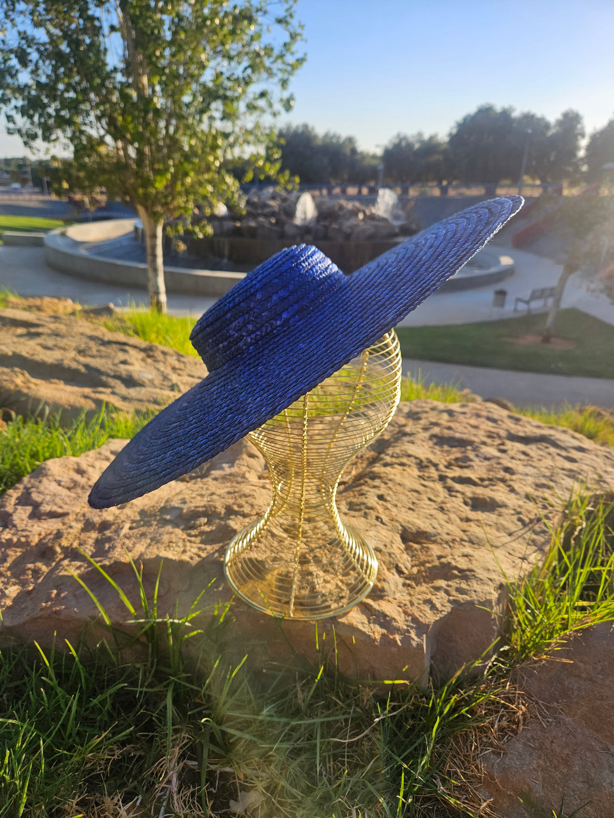 Sombrero de paja azul con ala ancha y trenzado, sobre maniquí dorado.