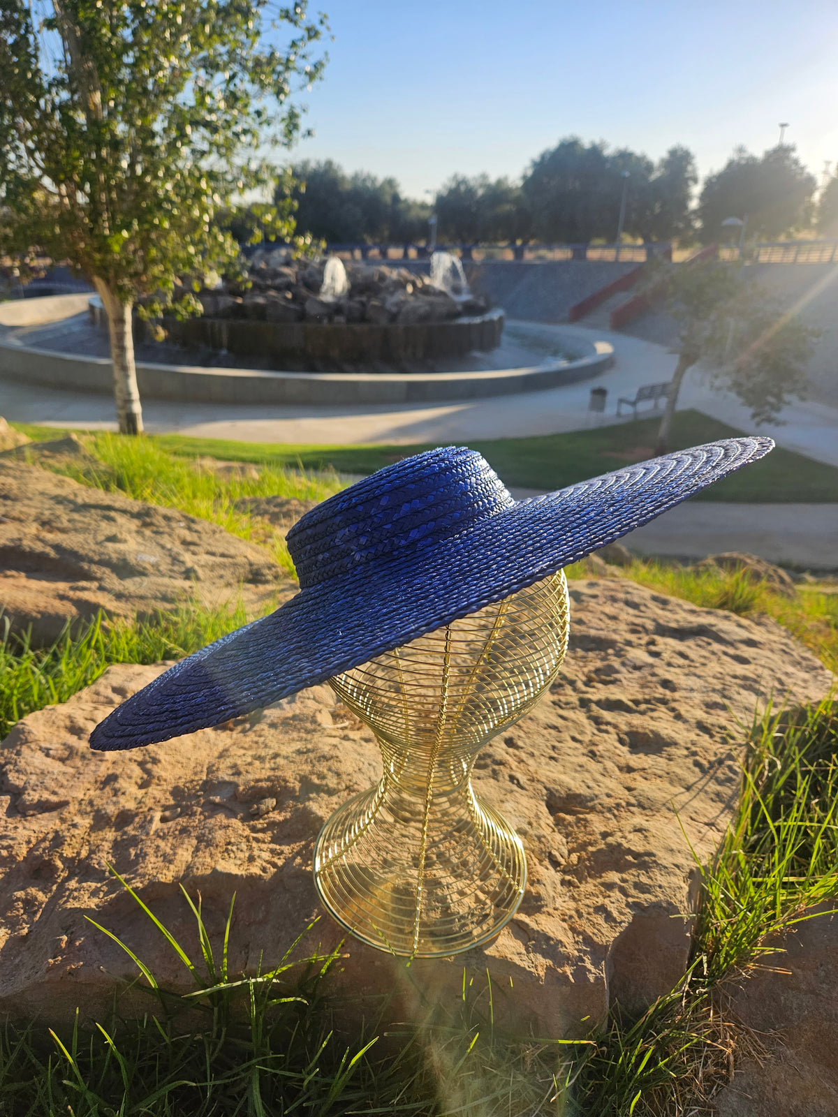 Sombrero de paja azul con ala ancha, vista lateral sobre maniquí dorado.