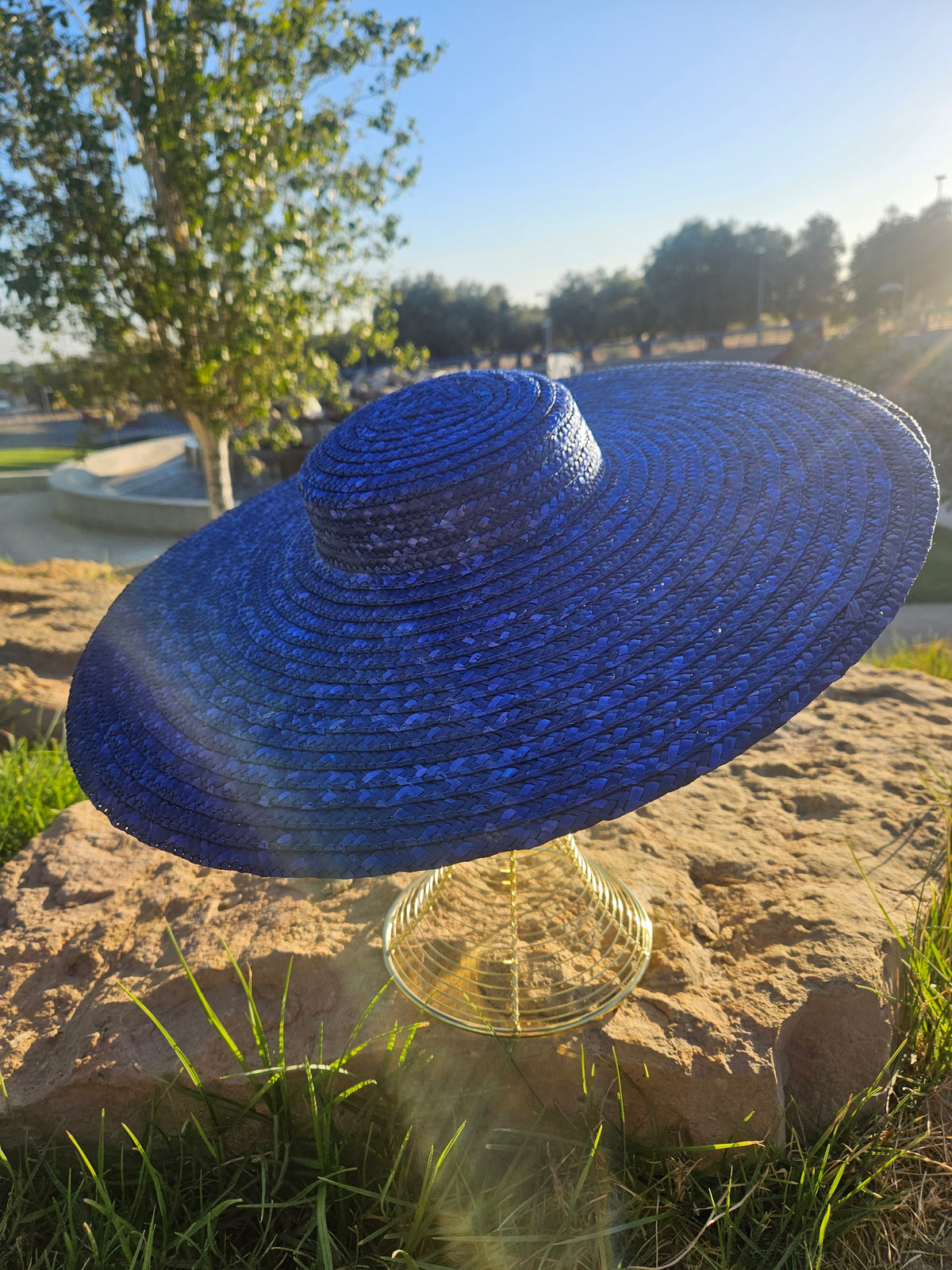 Sombrero de paja azul con ala ancha y copa abombada, sobre maniquí dorado.
