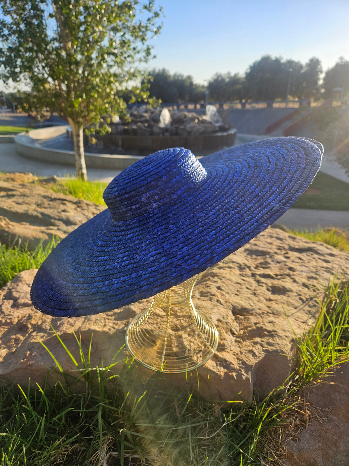 Sombrero de paja azul con ala ancha, vista diagonal sobre maniquí dorado.