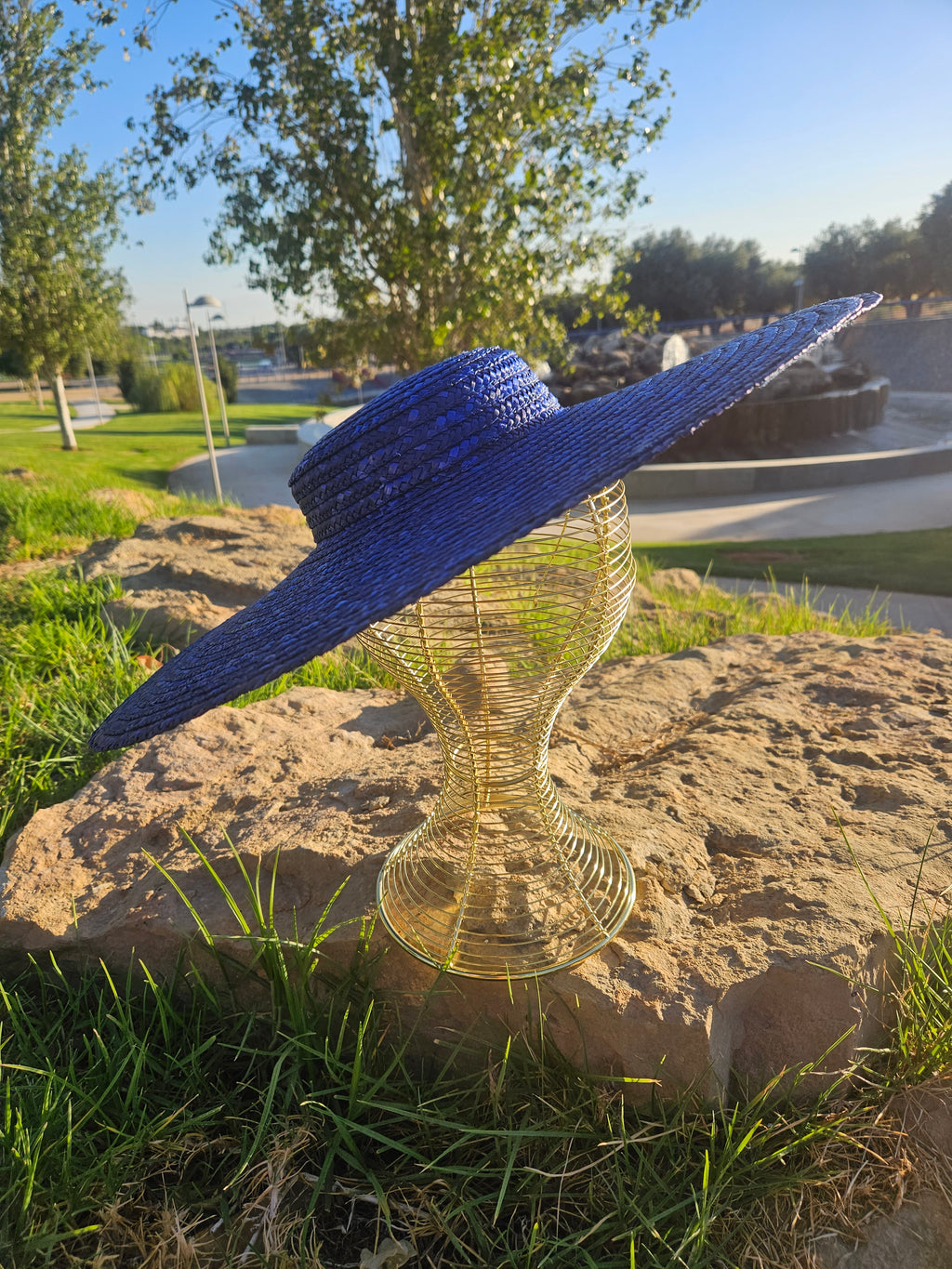 Sombrero de paja azul con ala ancha, vista trasera sobre maniquí dorado.