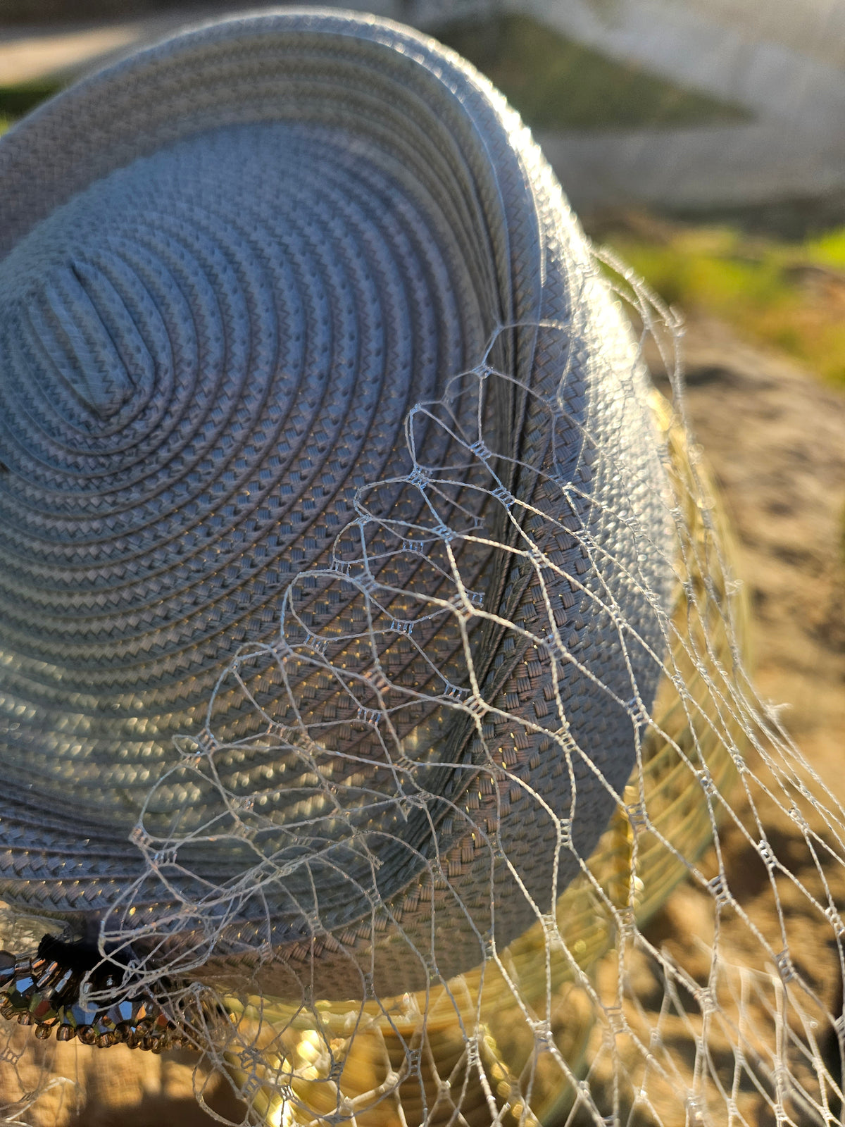 Sombrero azul con velo de malla y adorno de cuentas negras en el lateral.