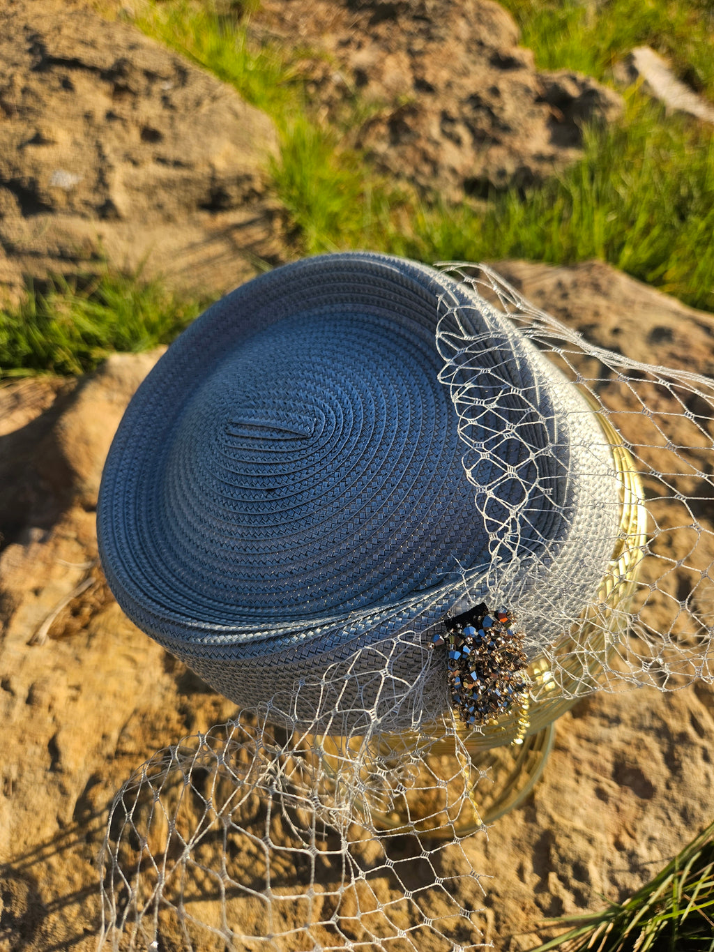Sombrero azul con ala pequeña, velo de malla dorada y pieza frontal con cuentas negras.