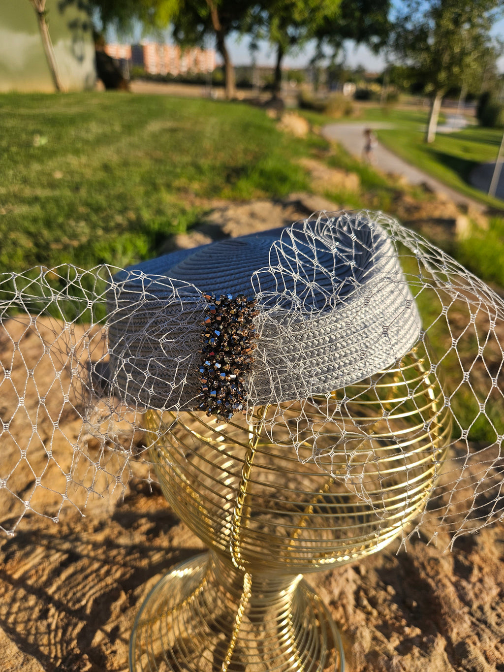 Sombrero azul con tocado de malla dorada, velo y cuentas negras en la banda.