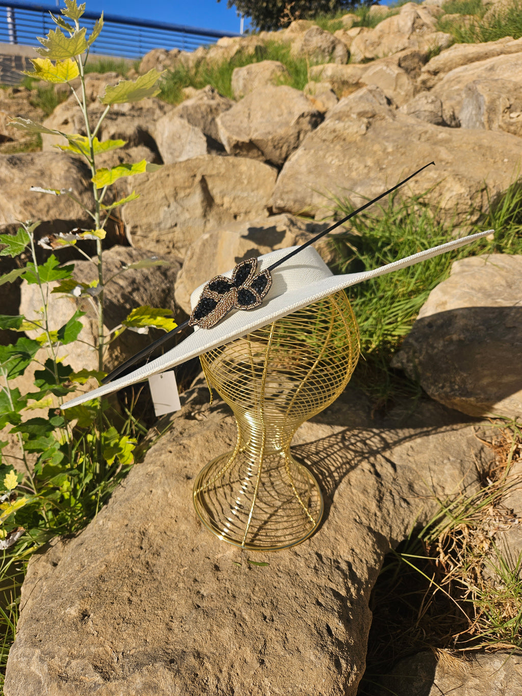 Sombrero de ala ancha claro con adorno mariposa negro y dorado sobre cinta negra