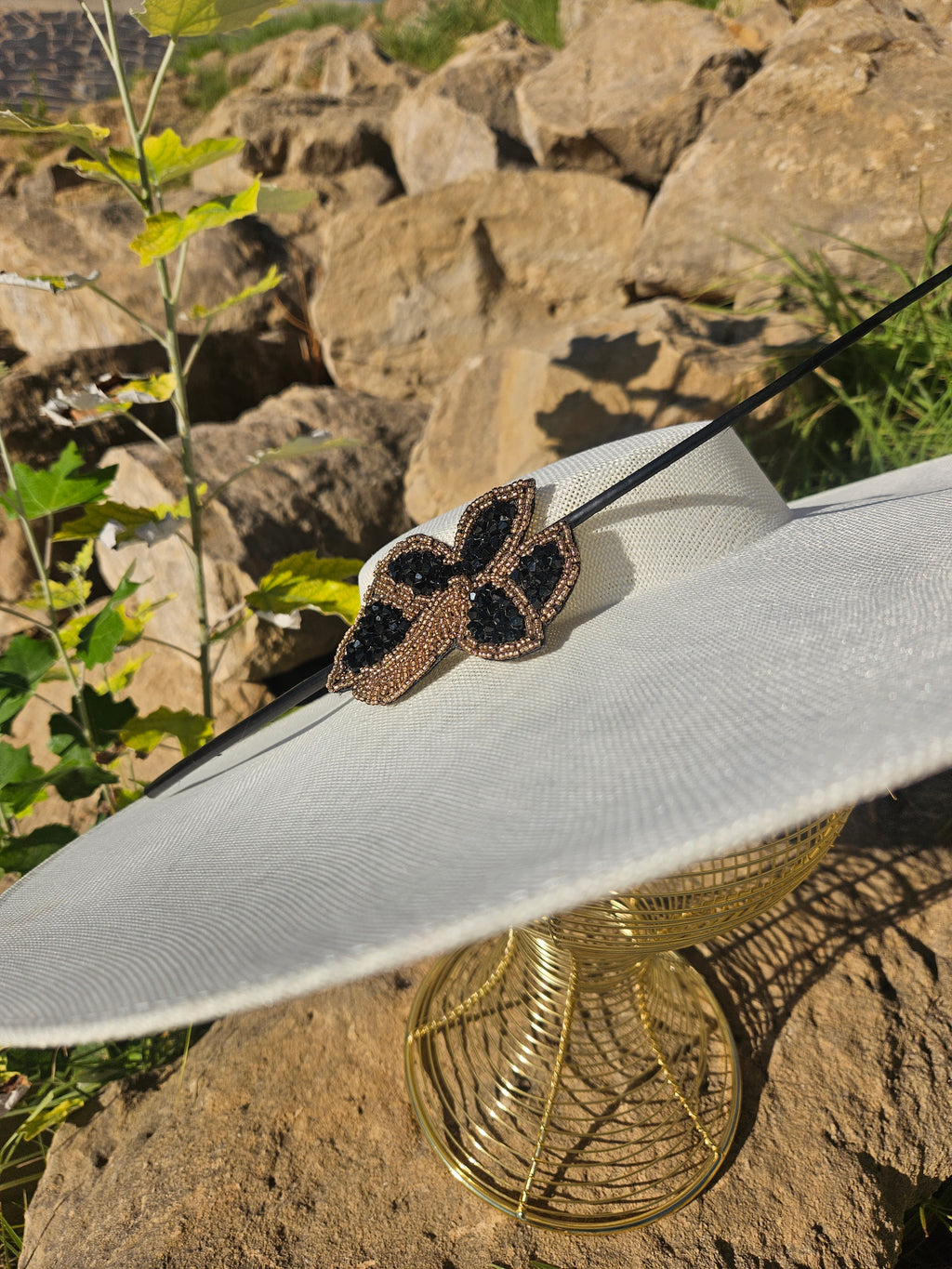 Sombrero de ala ancha claro con adorno mariposa negro y dorado y cinta negra