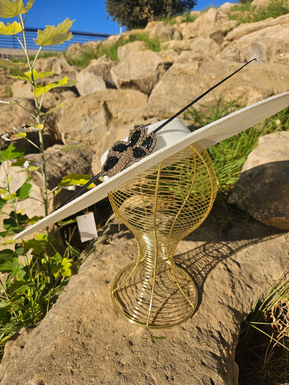 Sombrero de ala ancha claro con adorno mariposa negro y dorado y cinta negra