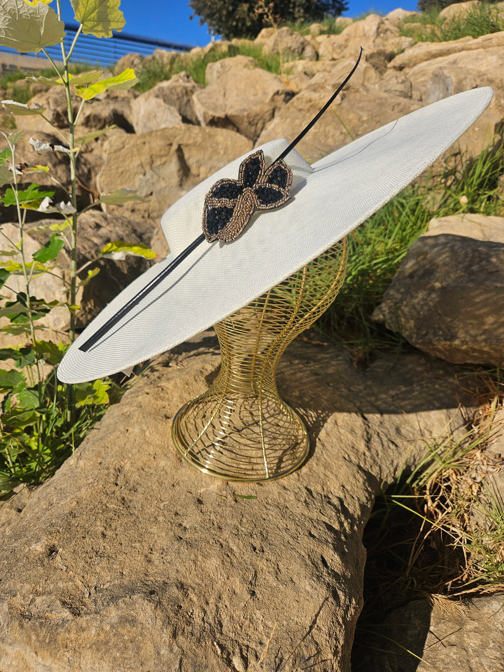 Sombrero de ala ancha claro con adorno mariposa negro y dorado sobre cinta negra
