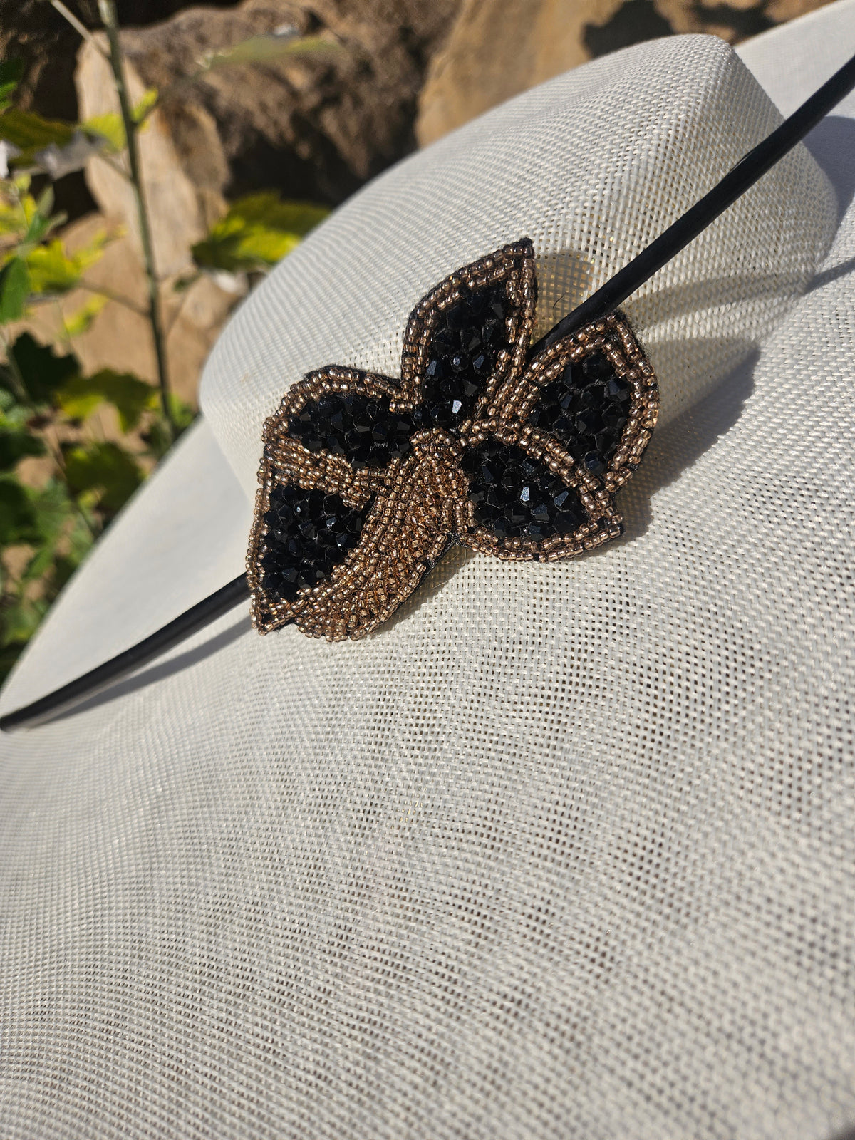 Sombrero de ala ancha color claro con adorno mariposa negro y dorado en la cinta