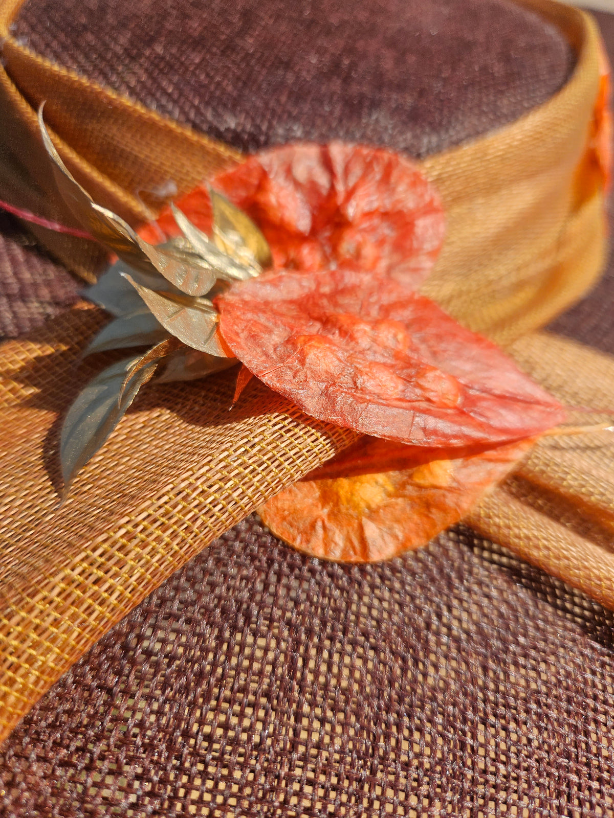 Pamela de ala ancha en tela marrón, con adorno floral naranja y detalles metálicos